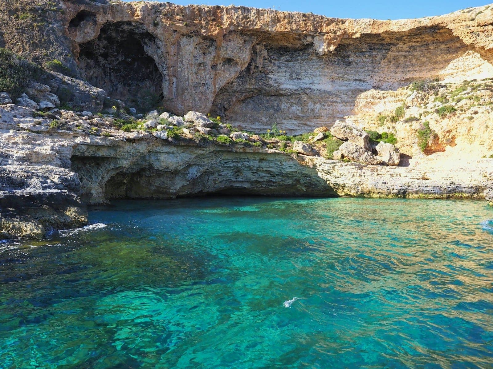Klares türkisfarbenes Wasser mit Felsklippen und einem Höhleneingang, typisch für Maltas beliebte Küstentauchplätze.