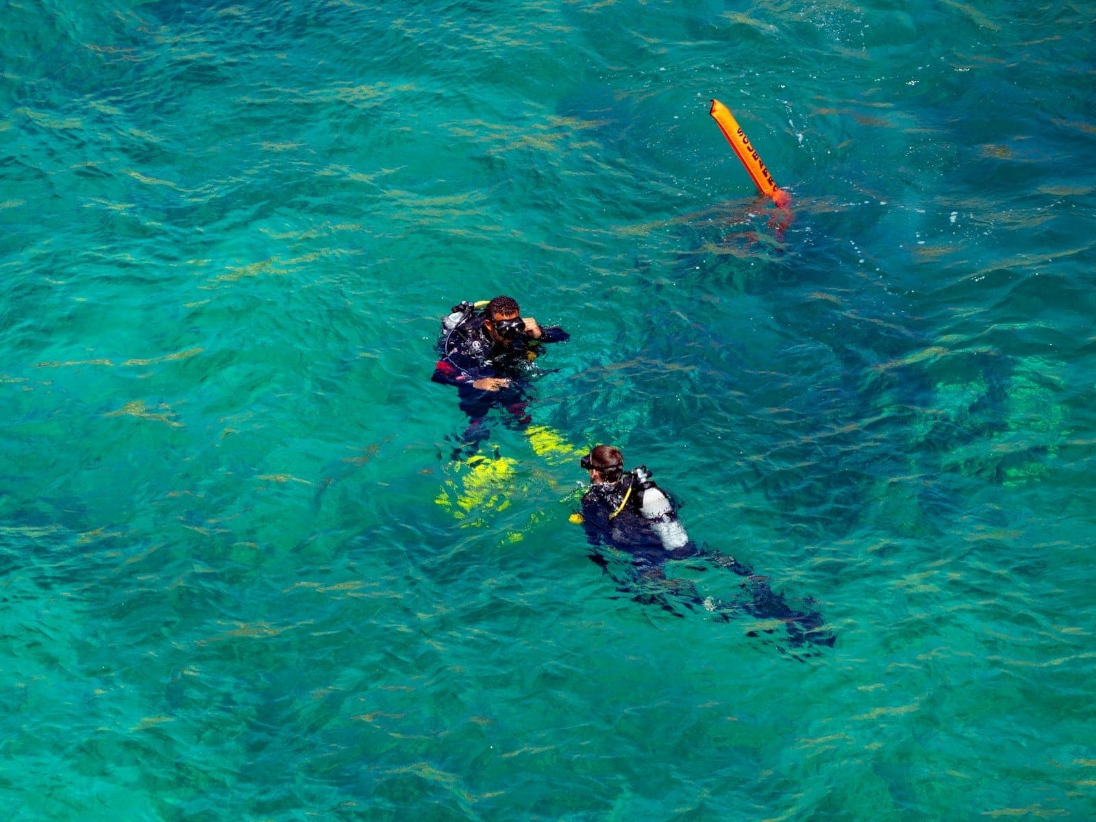Zwei Taucher schweben im türkisblauen Mittelmeerwasser nahe Malta und bereiten sich mit ihrer Ausrüstung auf den Tauchgang vor – ein echter Abenteuerstimmung.
