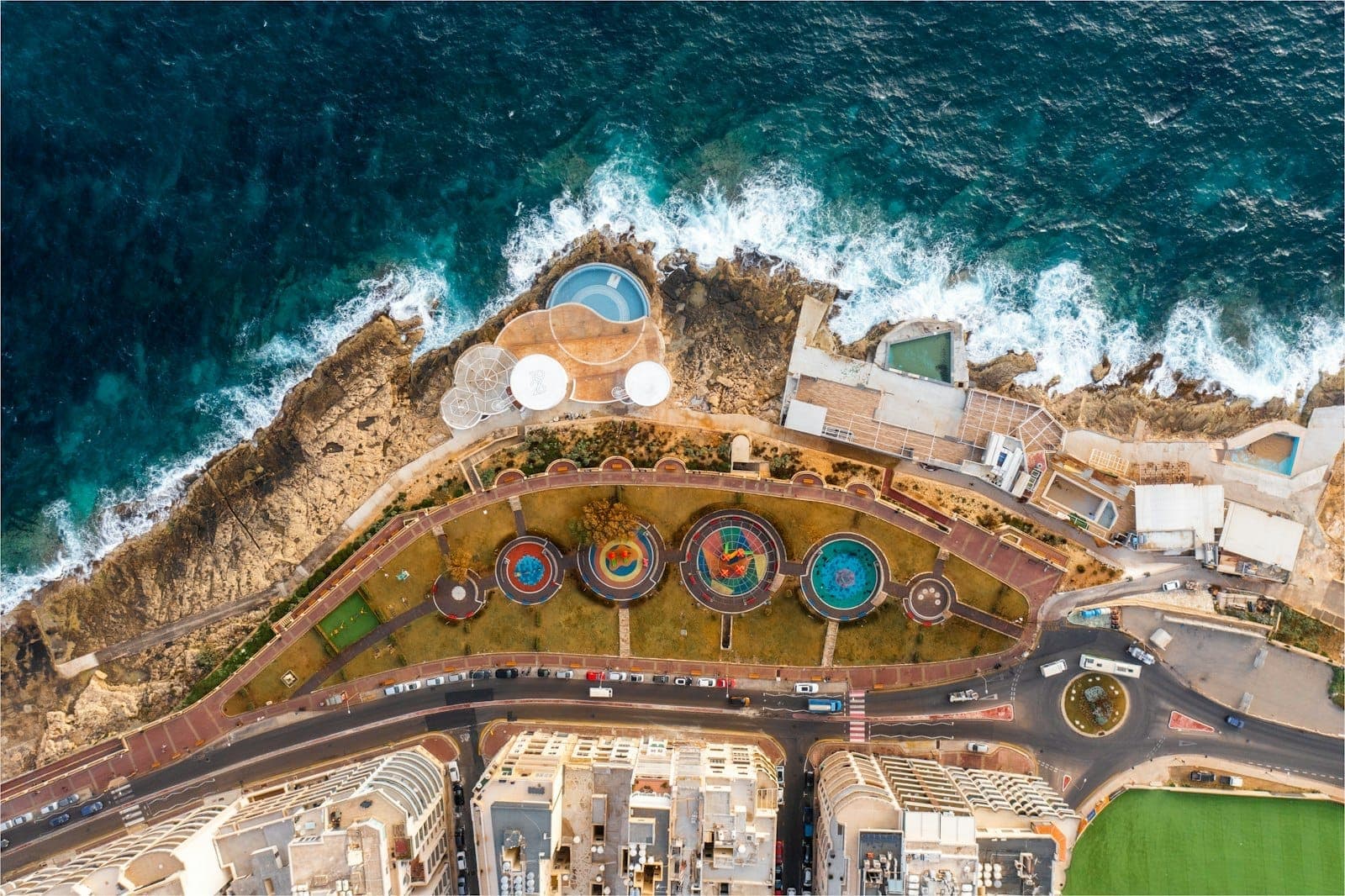 Luftaufnahme einer felsigen Küste mit Pools und Liegestühlen eines Beach Clubs am Meer in Malta