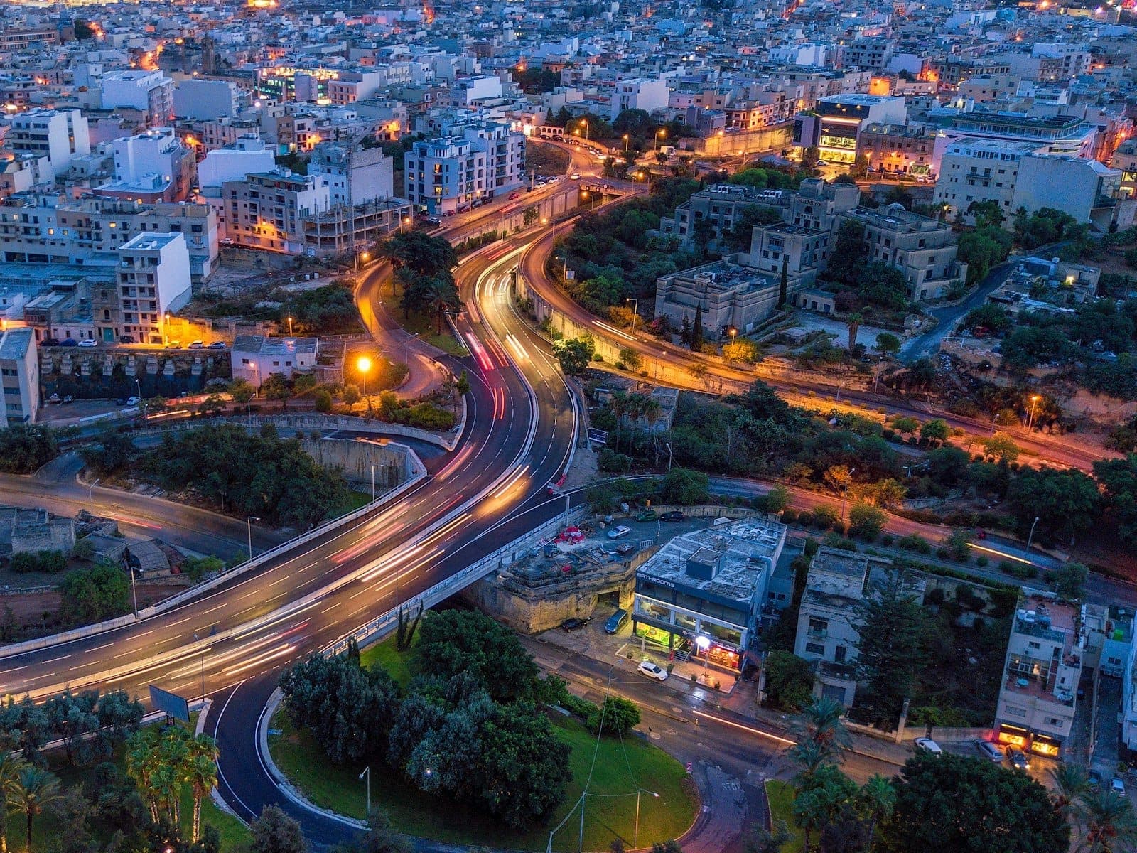Luftaufnahme der Stadtlandschaft von Malta bei Nacht mit beleuchteten Straßen und Gebäuden, die Ballungsräume des Nachtlebens und die Stadtgeographie zeigt.