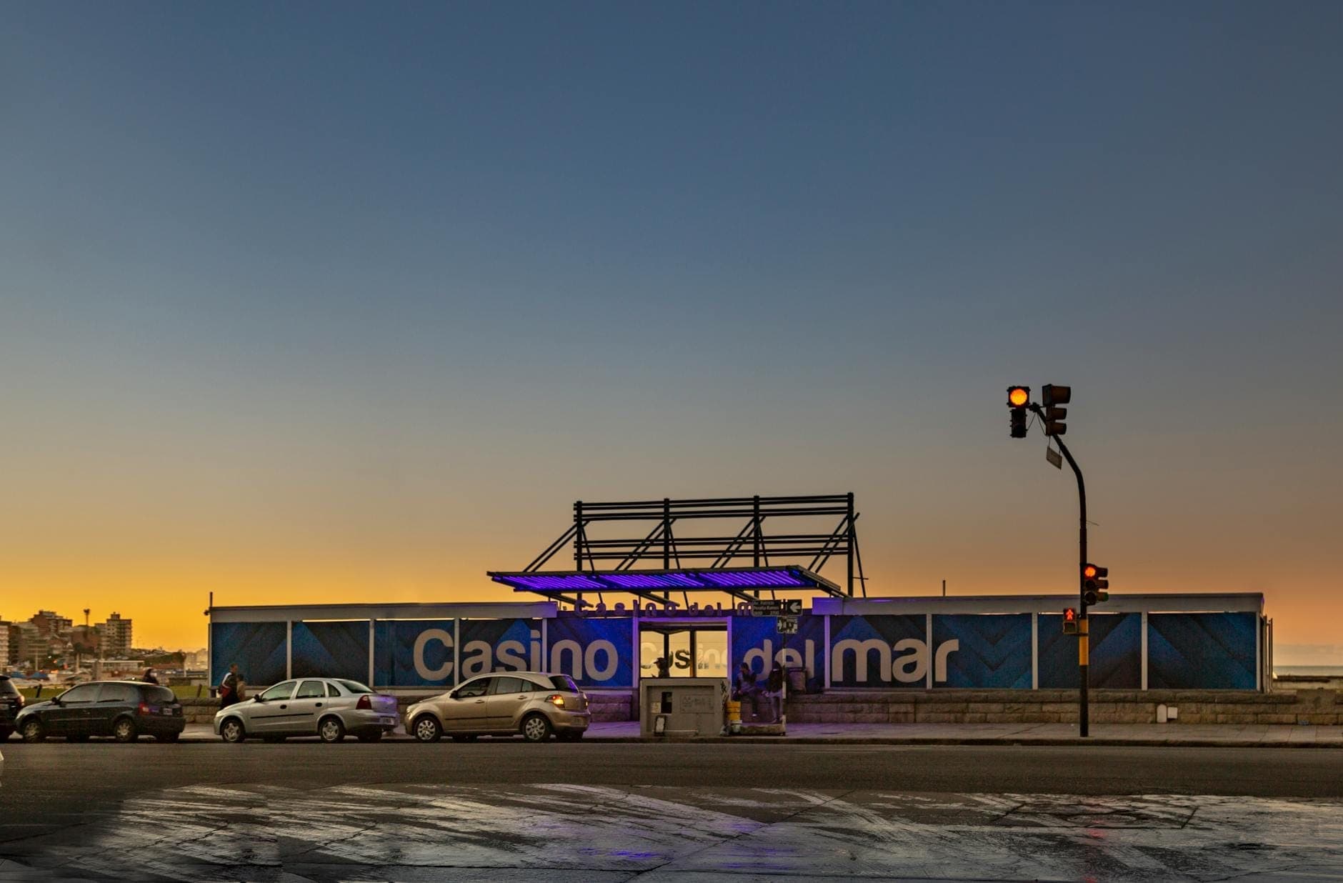 Außenansicht des Café del Mar Malta in der Abenddämmerung, mit Sonnenuntergangslicht und davor geparkten Autos, blaues Schild sichtbar.