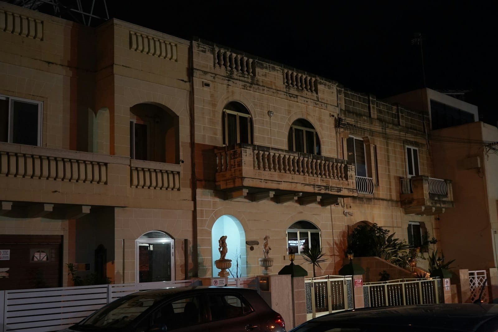Nachtansicht eines bescheidenen Gästehauses oder Budgethotels mit Balkonen und geparkten Autos davor, typisch für eine Unterkunft in Malta.