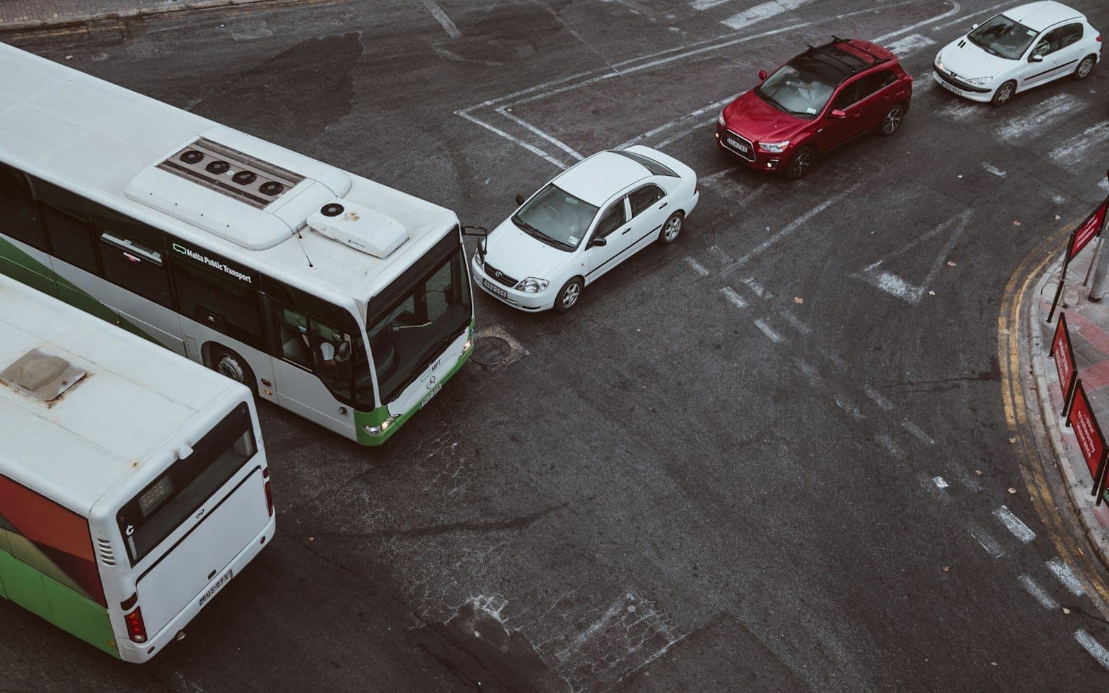 Un autobus pubblico e diverse auto fermi a un incrocio in una strada urbana di Malta con segnaletica orizzontale visibile.