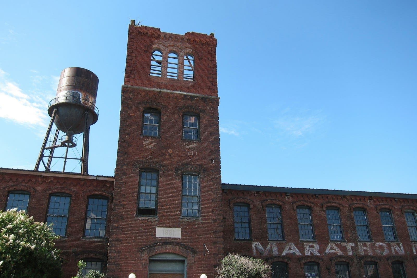 Historic red brick Marathon Village factory in Nashville with tall windows, weathered water tower, and clear blue sky in the background.