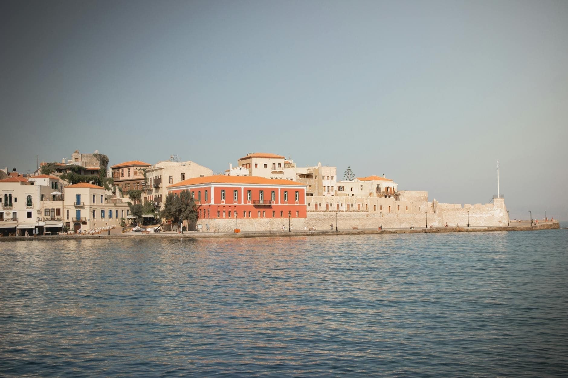 Blick auf den venezianischen Hafen von Chania mit der Firka-Festung und dem Maritimen Museum, im ruhigen Wasser gespiegelt unter einem sanften Himmel.