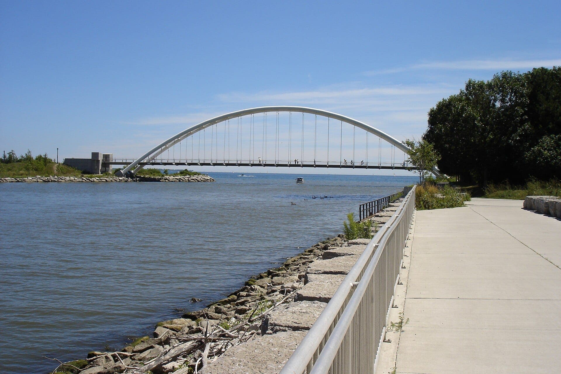 Il Martin Goodman Trail segue un percorso pavimentato lungo il lago Ontario, con il bianco Humber Bay Arch Bridge che attraversa acque calme e azzurre sotto un cielo sereno.