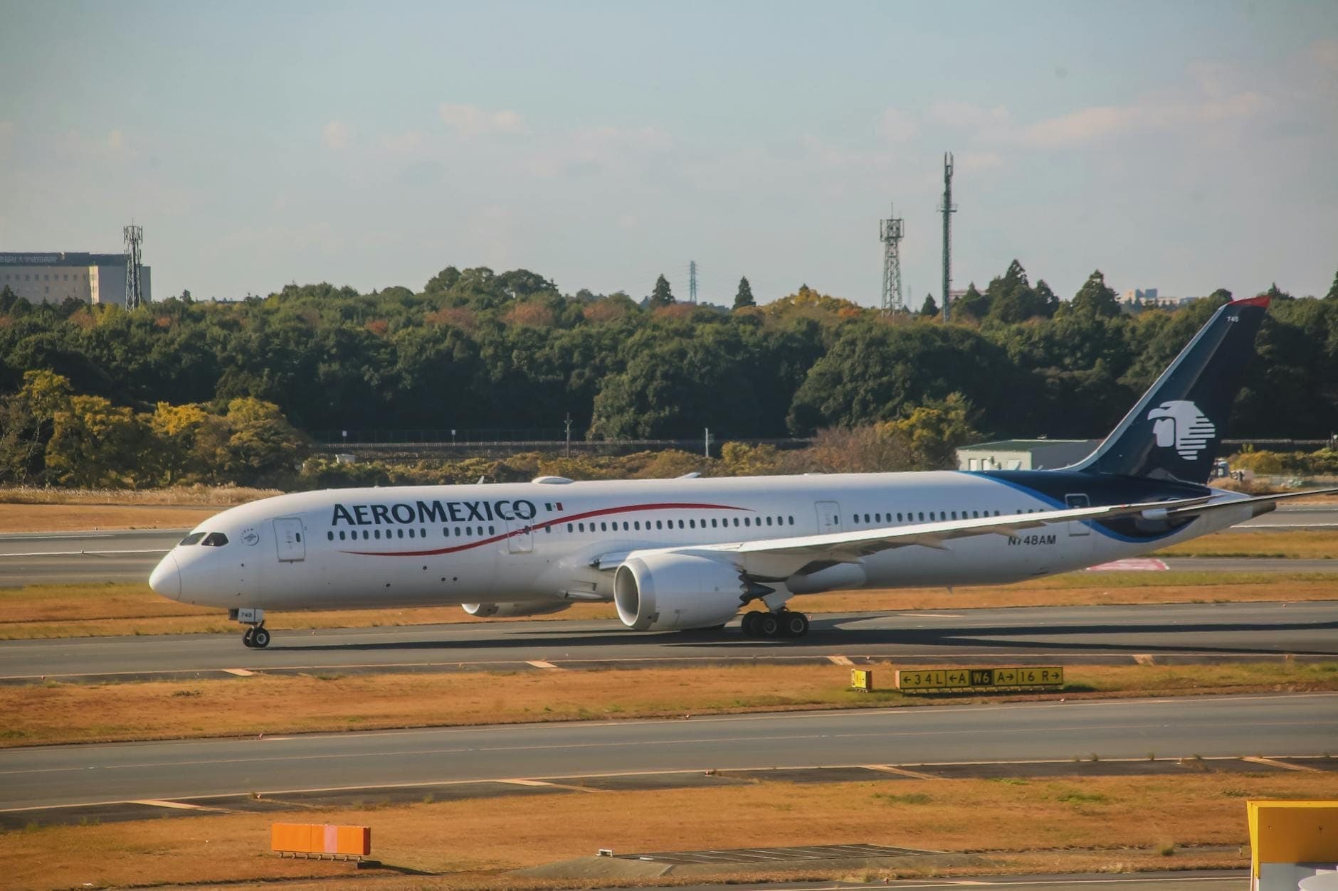 เครื่องบิน Aeromexico วิ่งบนรันเวย์ในสนามบิน ท่ามกลางต้นไม้และสิ่งปลูกสร้างใต้ท้องฟ้าแจ่มใส