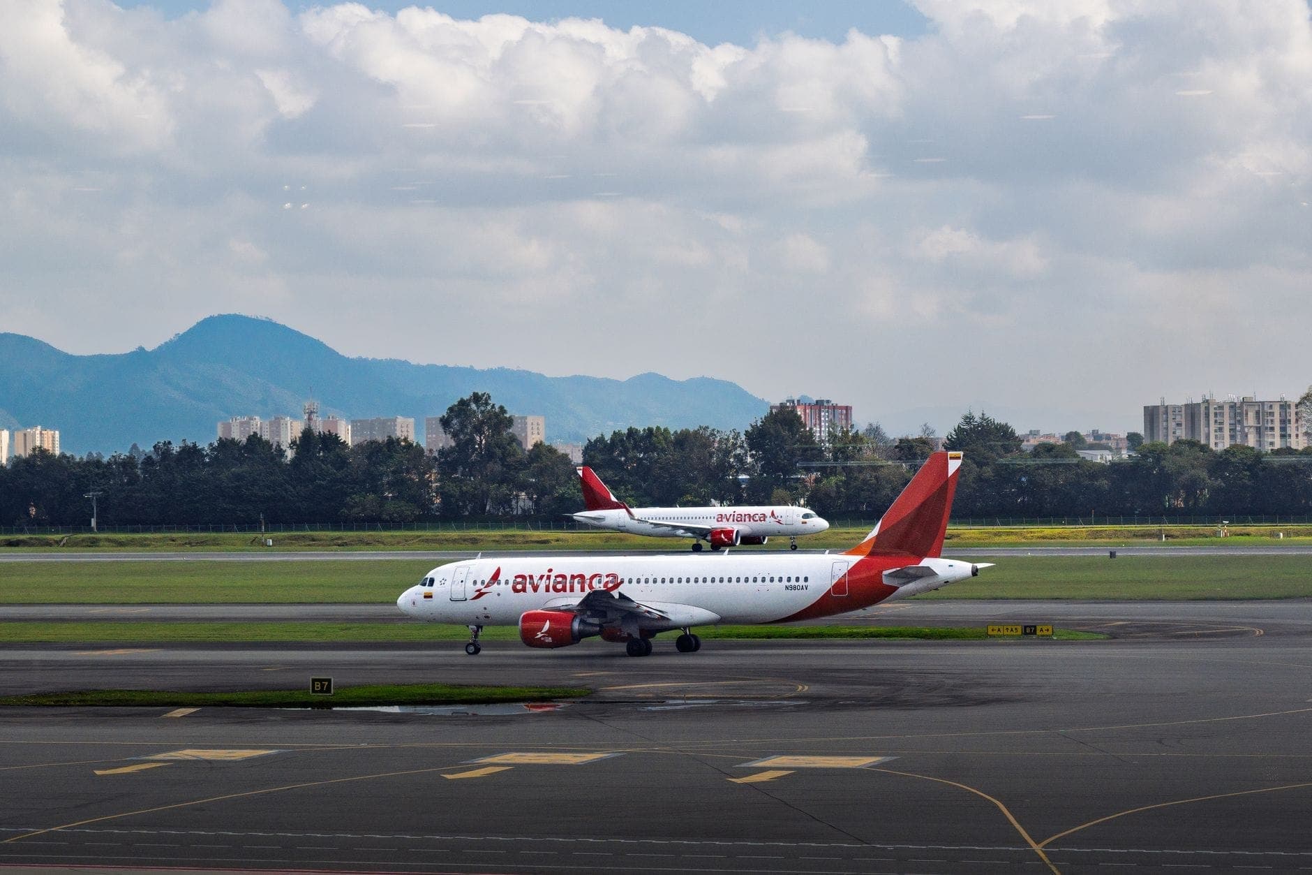 Two Avianca airplanes on the tarmac with Mexico City’s skyline and mountains in the background, viewed from the airport.