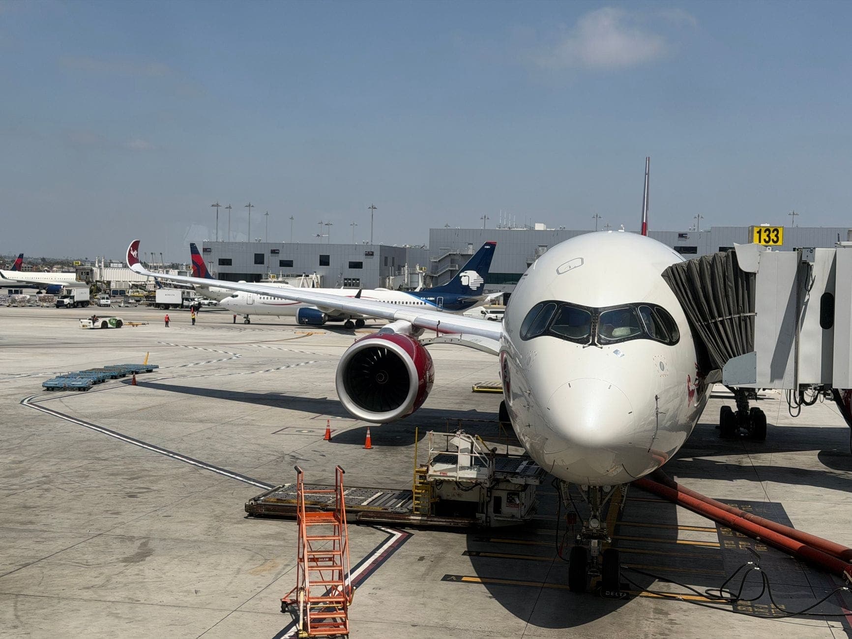 Wide view of a modern airport gate with a large airplane at the jet bridge and other planes in the background.