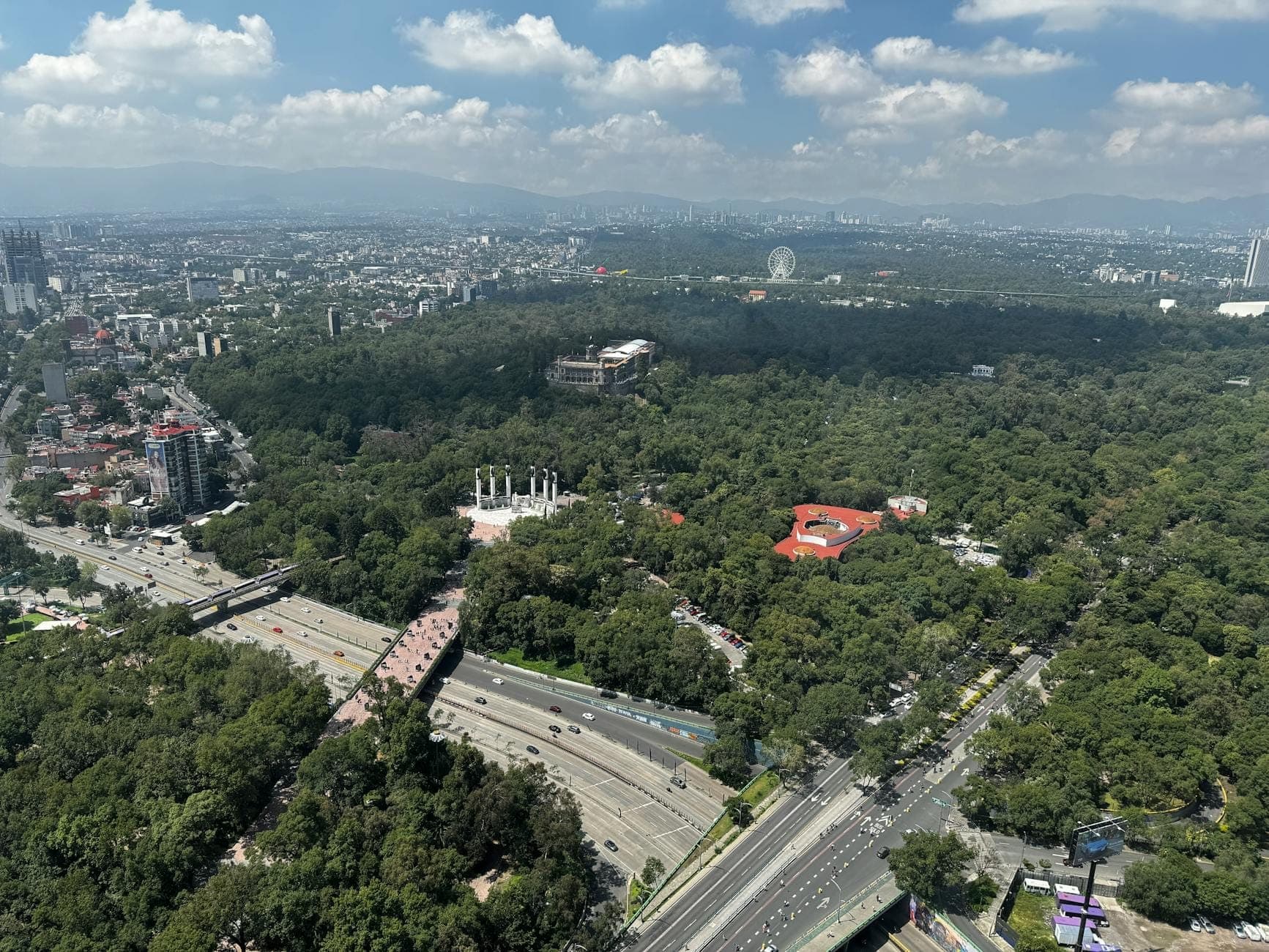Vista aerea di Mexico City con il Chapultepec Park, gli edifici della città e le montagne sullo sfondo sotto un cielo parzialmente nuvoloso