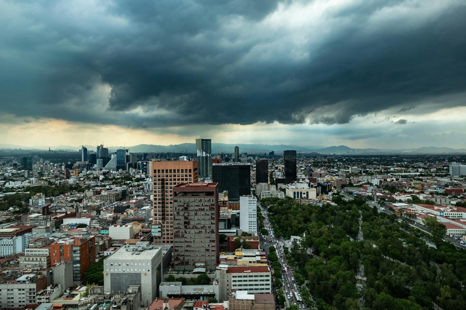 Ampia veduta dello skyline di Mexico City con spettacolari nuvole della stagione delle piogge e aree verdi visibili nel paesaggio urbano.