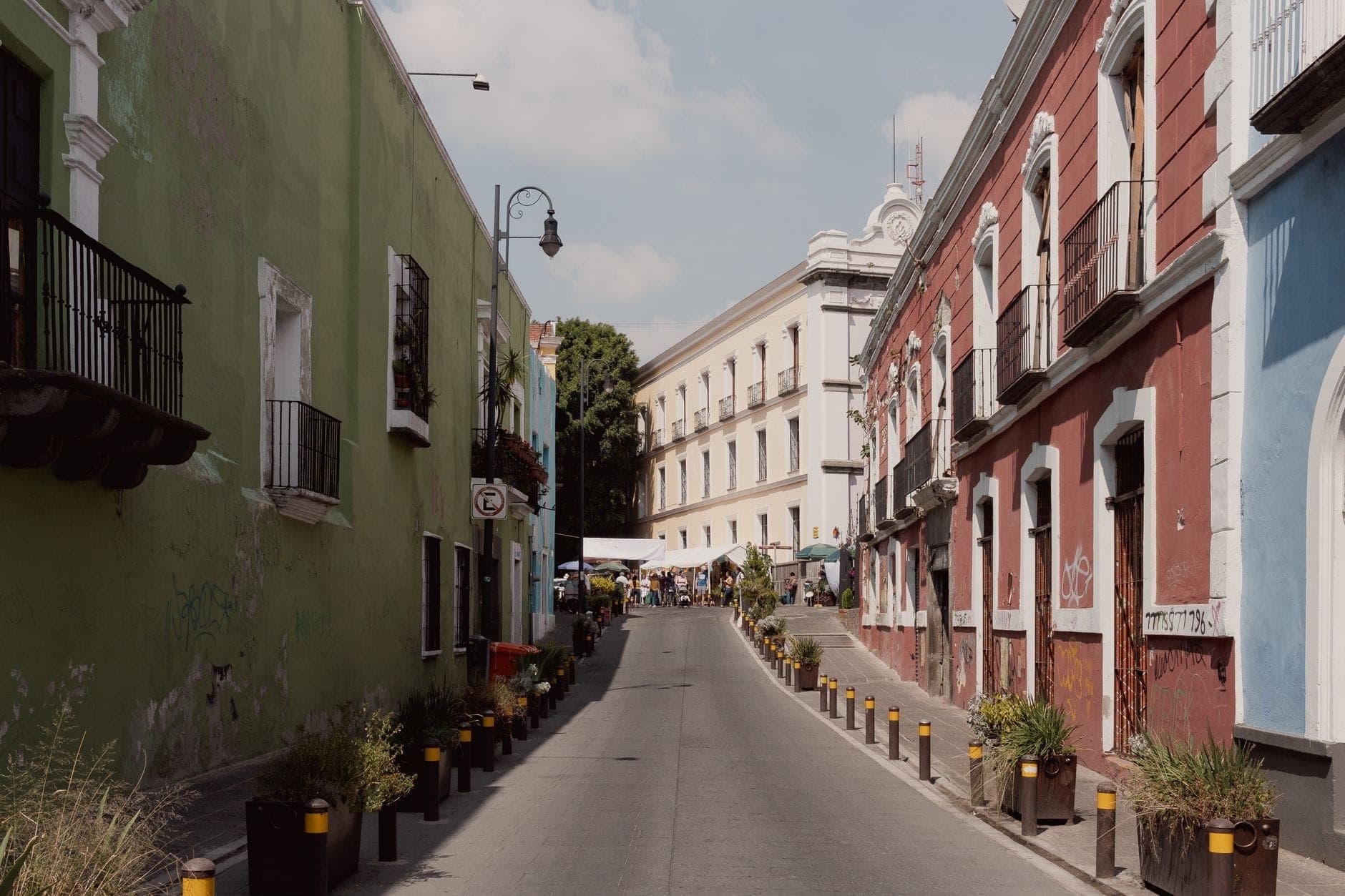 Encantadora calle estrecha en Ciudad de México flanqueada por coloridos edificios históricos y plantas en macetas, que evoca un ambiente de barrio acogedor y transitable.