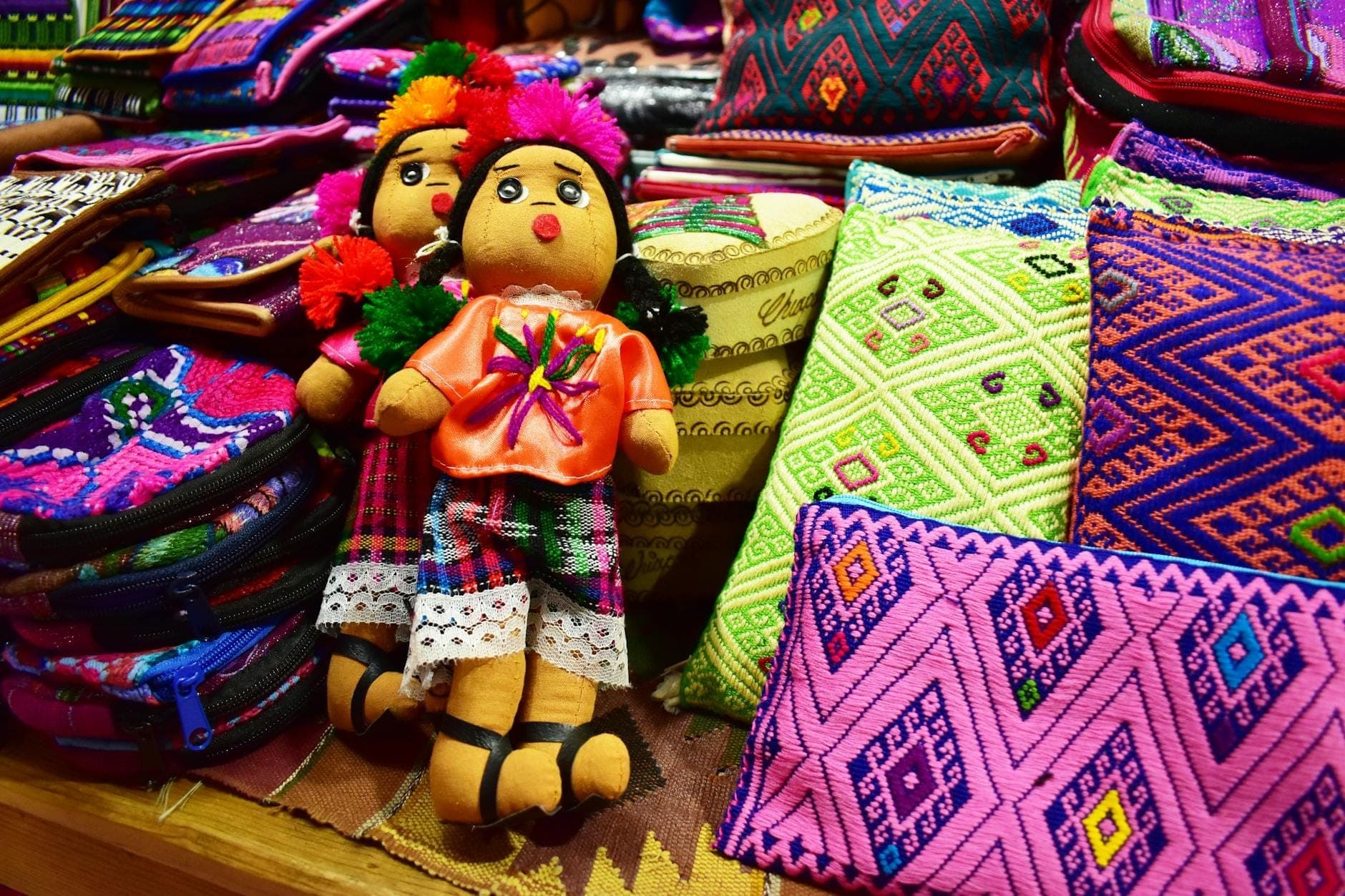 Colorful handmade Mexican dolls and textiles on display at a craft market stall.