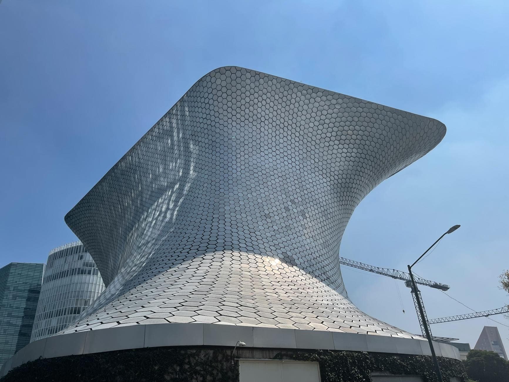 Modern silver hexagonal-tiled building of Museo Soumaya in Polanco with blue sky and some nearby skyscrapers.