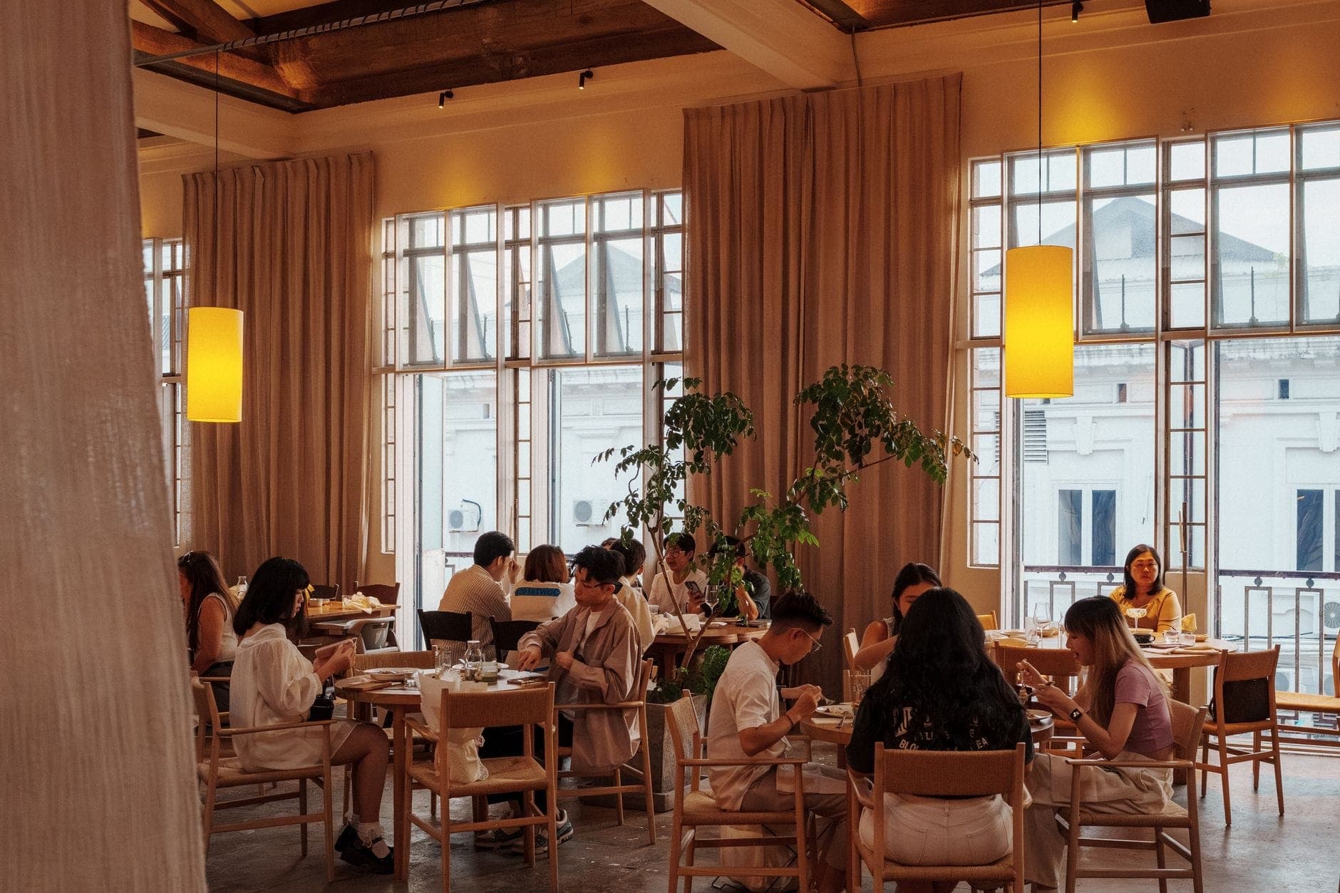Interior de restaurante de lujo a la luz del día con grandes ventanales, iluminación elegante, mobiliario moderno y comensales disfrutando de sus comidas en un ambiente animado.