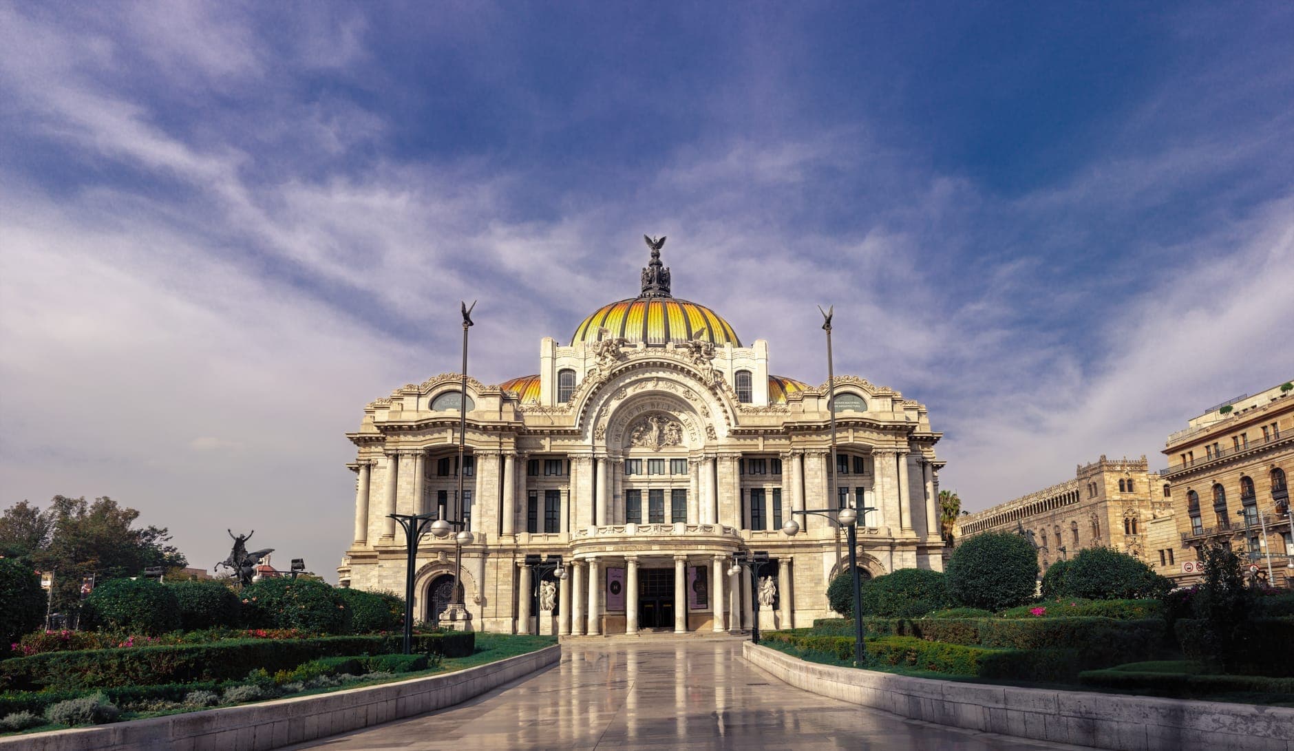 Wide angle view of Palacio de Bellas Artes in Mexico City under a blue sky, showing its grand architecture and surrounding gardens.