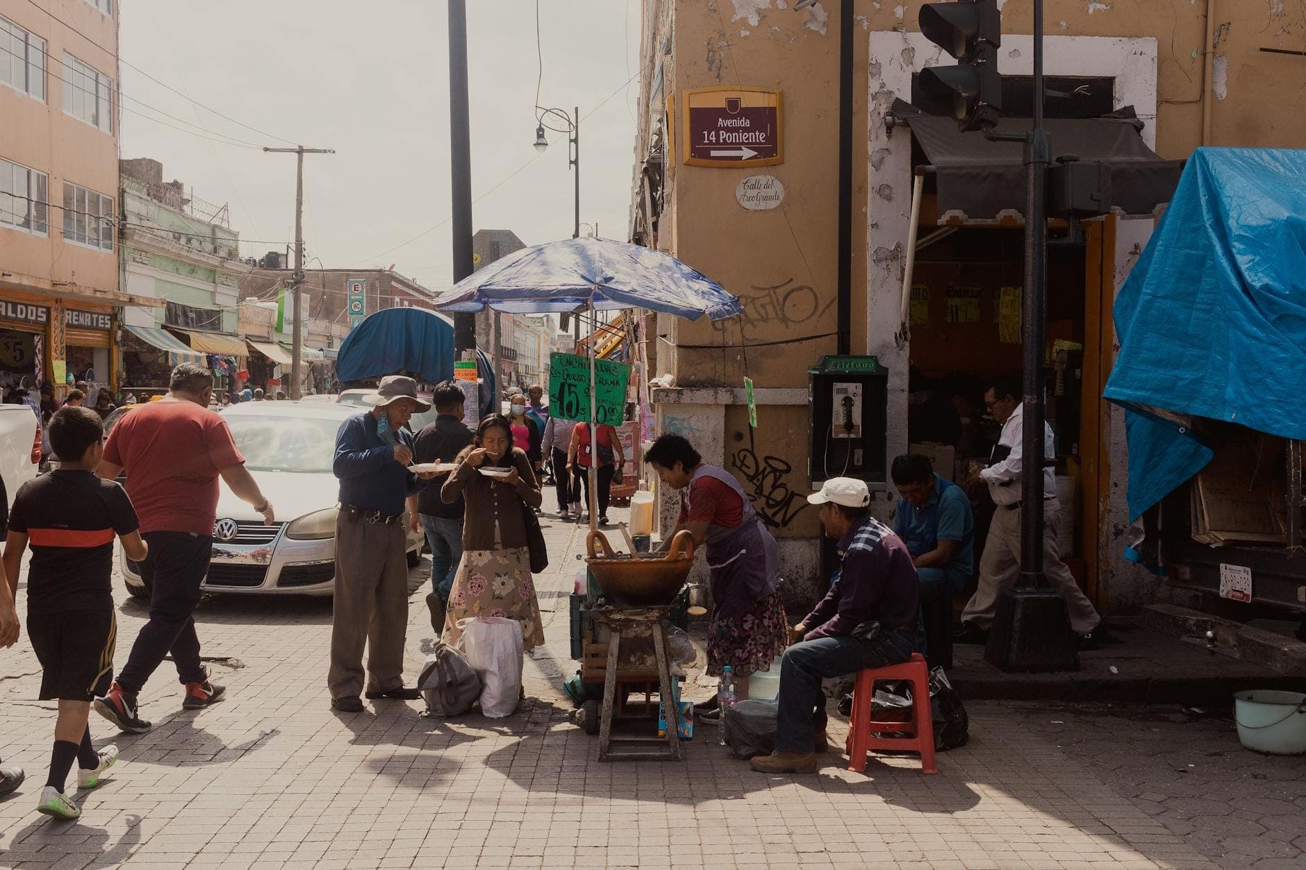 Escena callejera con personas reunidas alrededor de un puesto de comida bajo una sombrilla en una concurrida acera de Ciudad de México