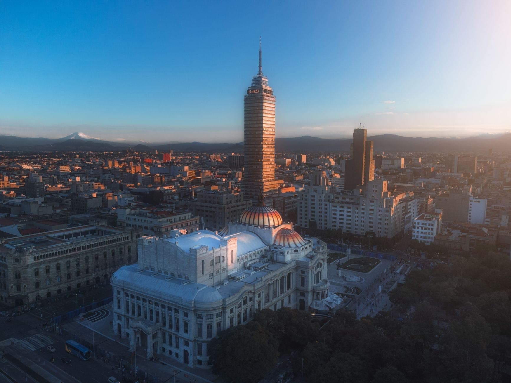 ภาพมุมสูงของเม็กซิโกซิตี้ยามเช้า มีตึก Torre Latinoamericana, Palacio de Bellas Artes, ฉากหลังเป็นภูเขาและท้องฟ้าหลากสี