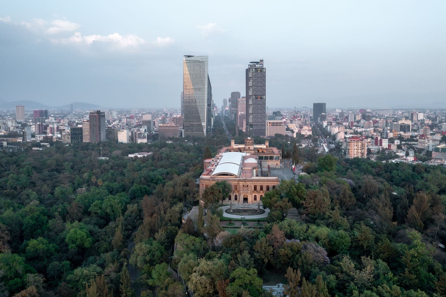 Widok z lotu ptaka na Castillo de Chapultepec otoczony zielonymi terenami parkowymi z wieżowcami Mexico City w tle w pogodny dzień.