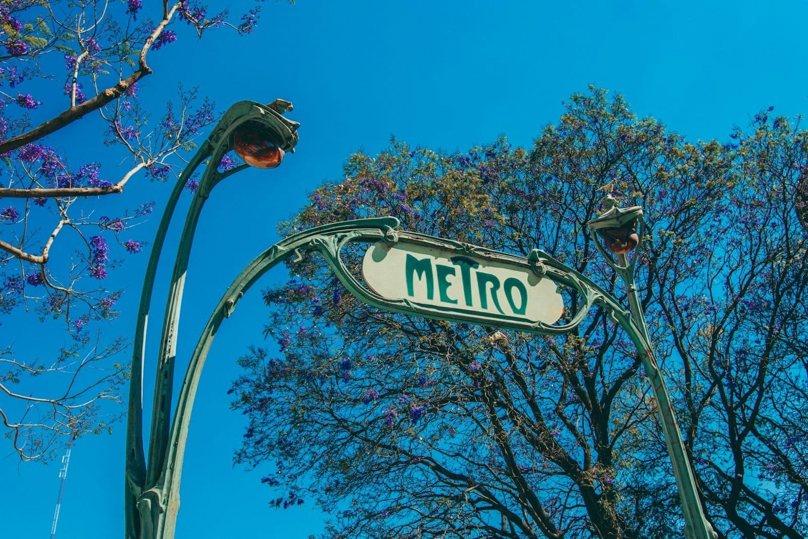 Art Nouveau metro entrance sign in Mexico City surrounded by trees and clear blue sky.