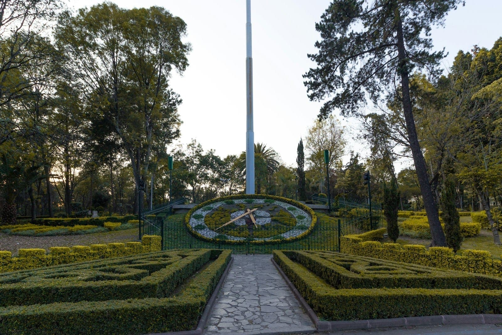 Large floral clock and manicured gardens in Chapultepec Park, surrounded by tall trees on a sunny day.