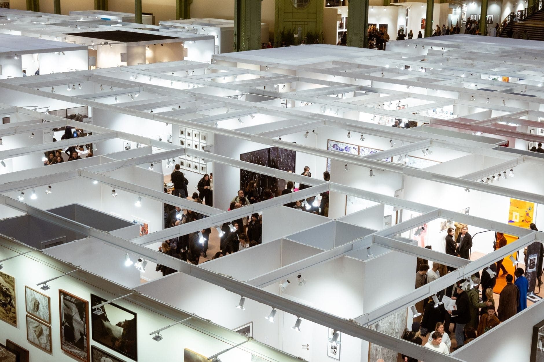 Wide view of a bustling contemporary art fair with white exhibition booths, crowds of visitors, and artwork displayed throughout a large gallery hall.