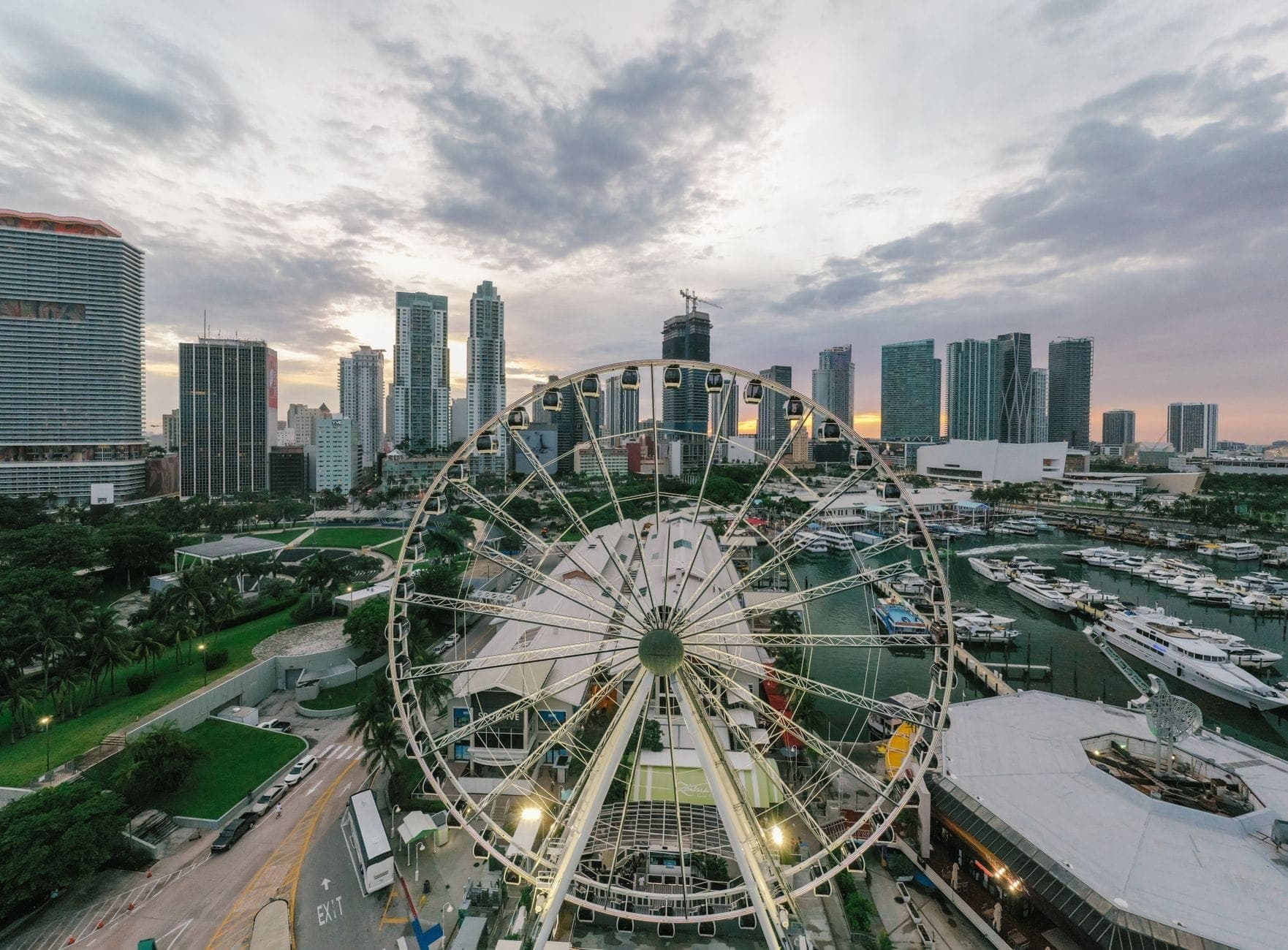 Large Ferris wheel with Miami downtown skyline and marina at sunset, evoking a lively urban atmosphere perfect for food tourism.