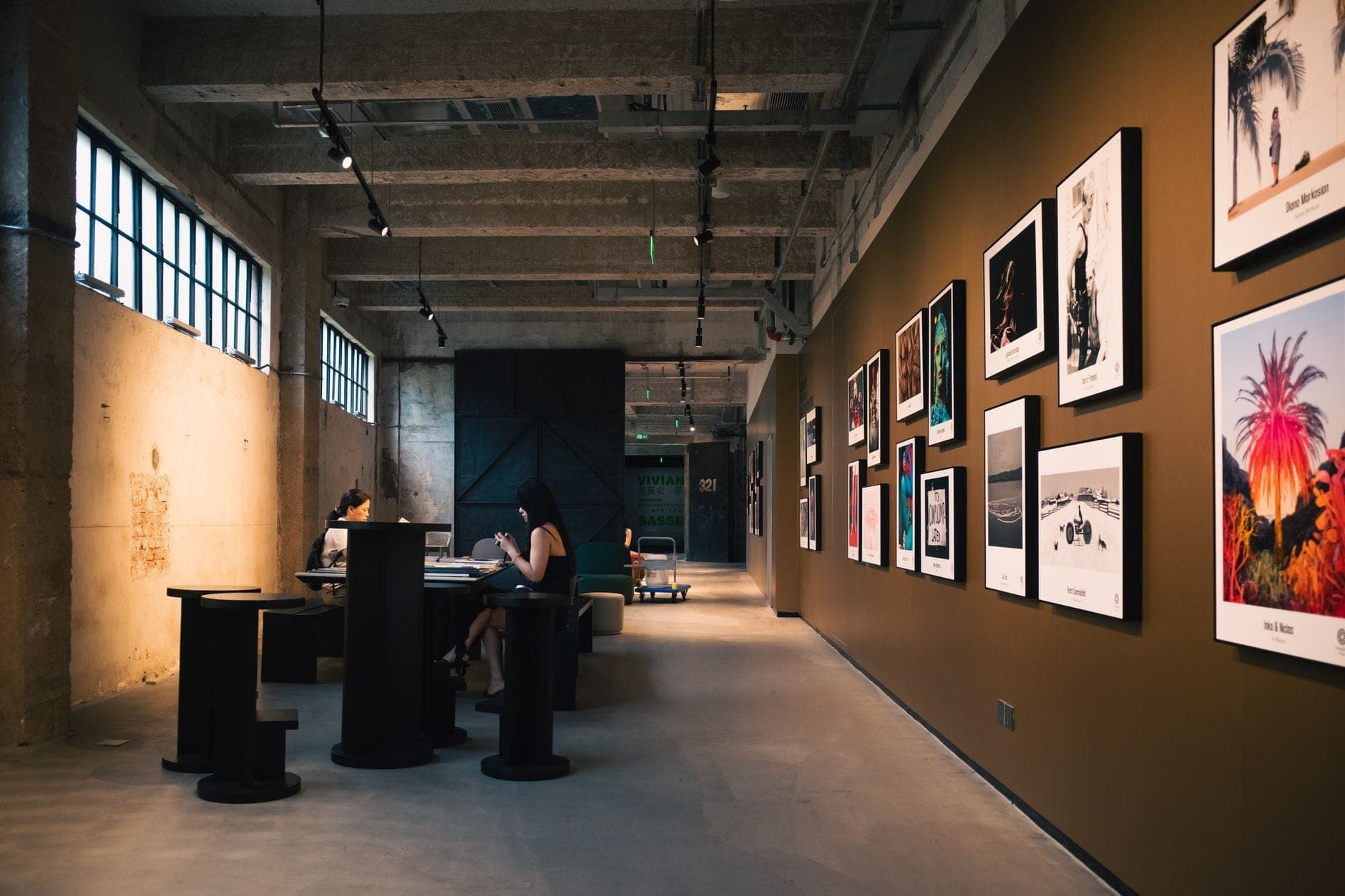 Contemporary art gallery with framed photographs and visitors, concrete and industrial design, warm lighting, and creative ambiance.