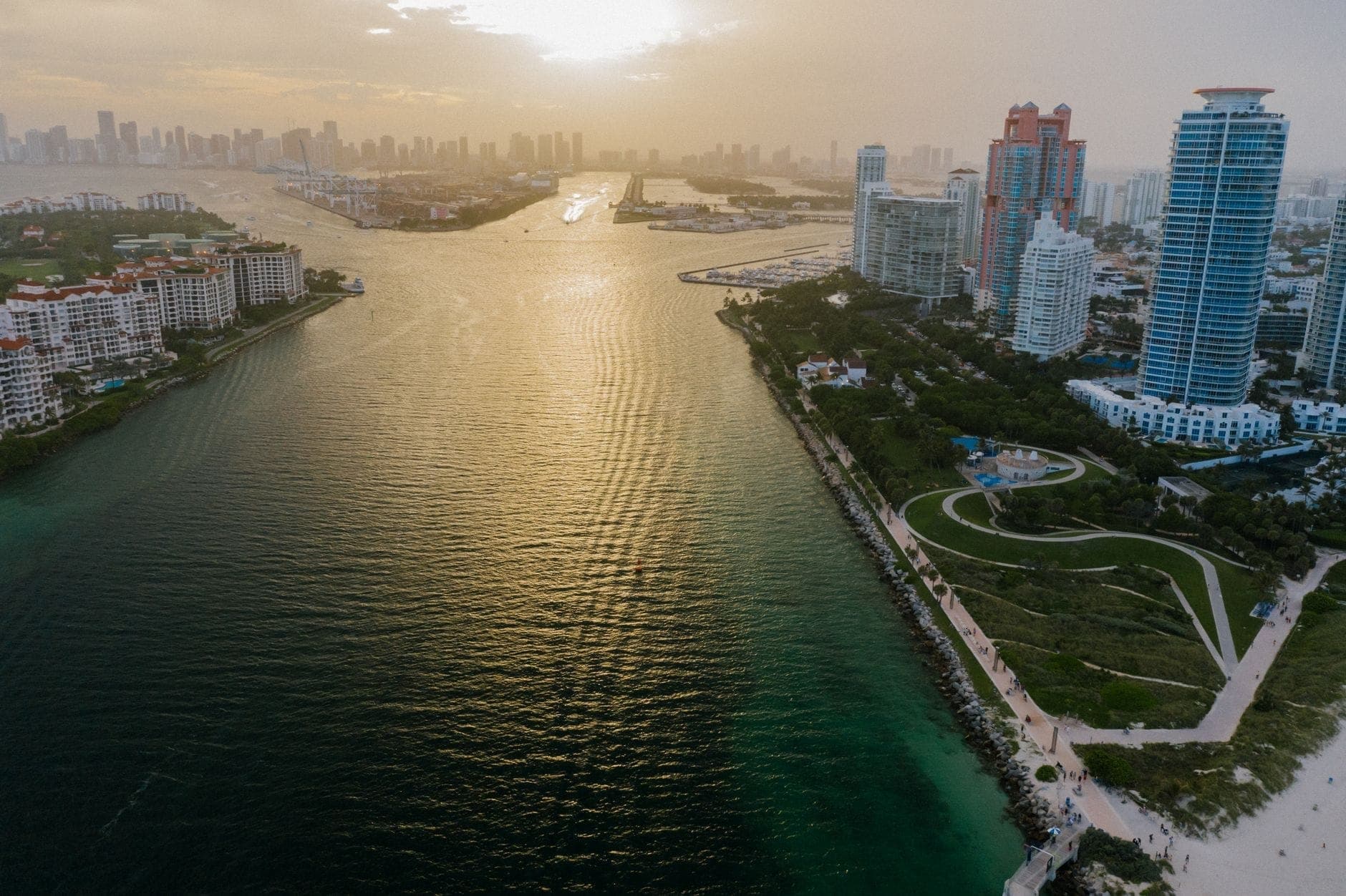 Vue aérienne des gratte-ciels de luxe en bord de mer de Miami et des quartiers huppés au coucher du soleil avec l'eau et la skyline de la ville en arrière-plan.