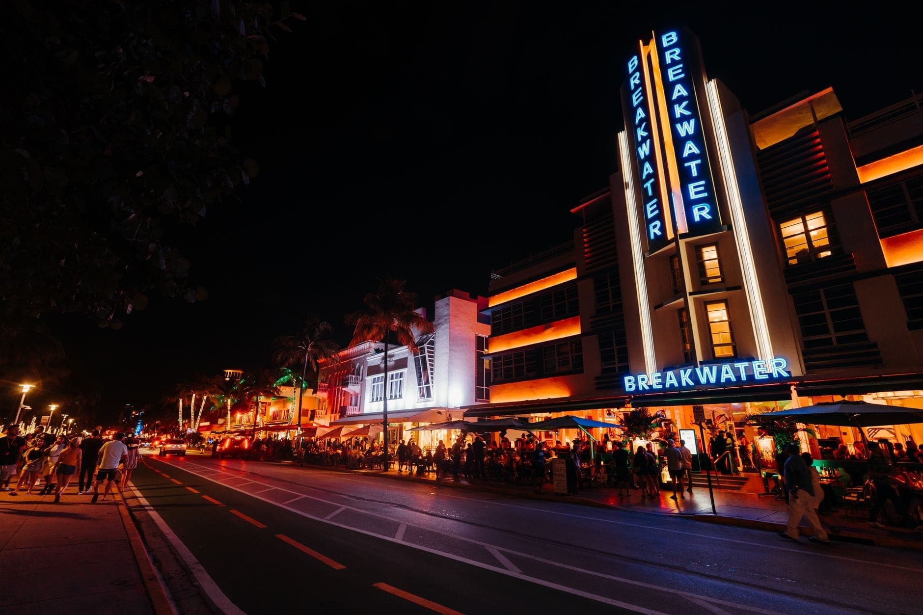 Оживлённая ночная жизнь Майами на Ocean Drive с неоновыми зданиями в стиле ар-деко, толпами людей и яркой клубной атмосферой ночью.