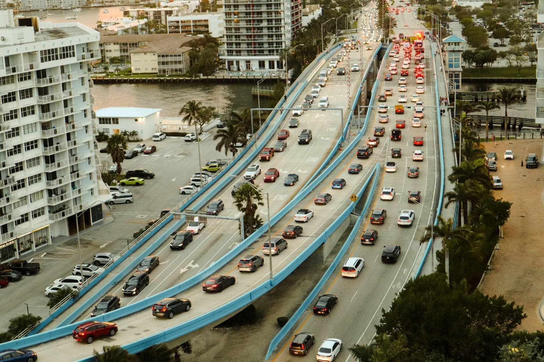 Aerial view of busy Miami causeway with heavy car traffic, palm trees, and surrounding city buildings during daylight.
