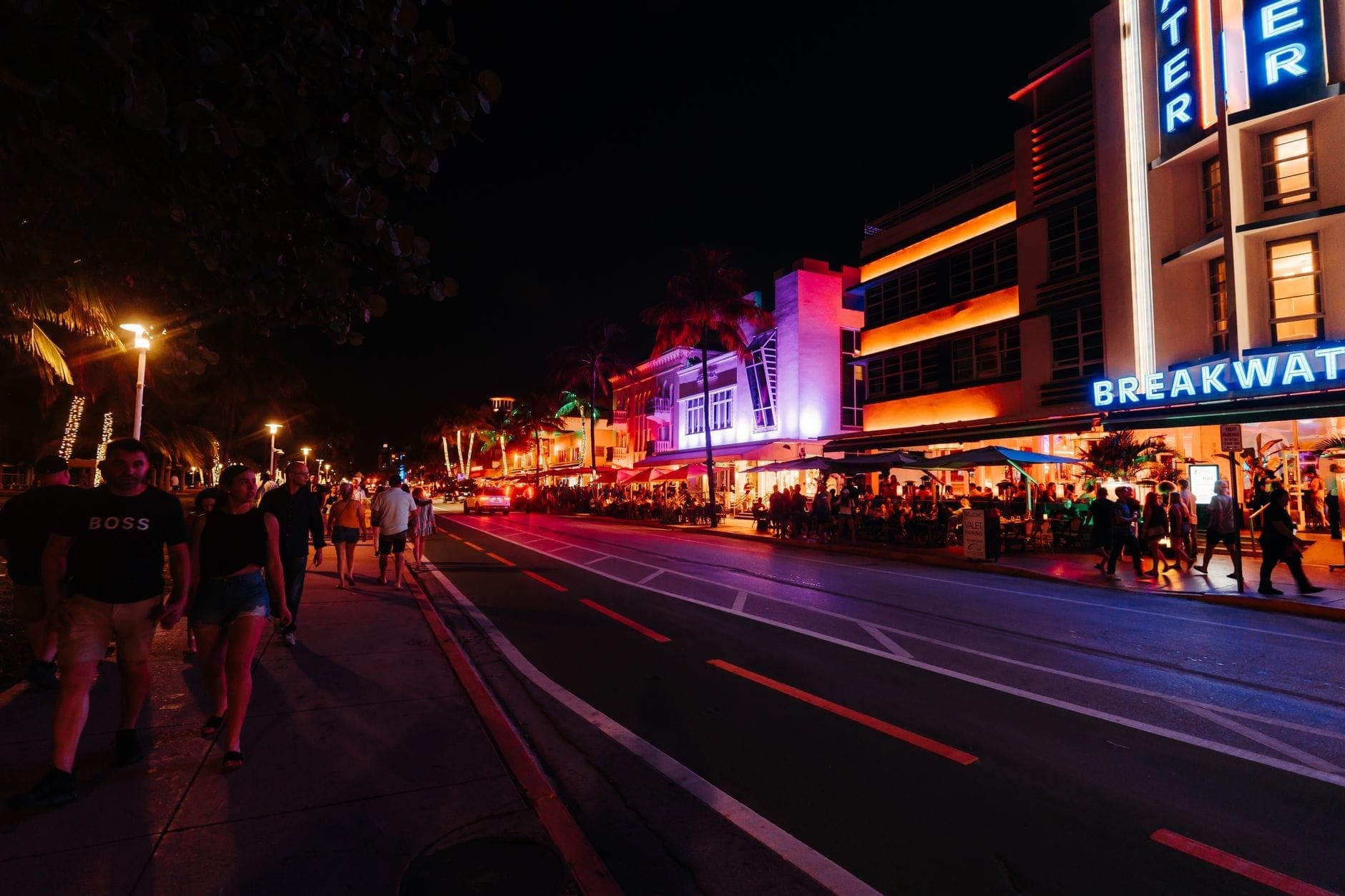 A lively Miami street scene at night with people walking, neon-lit Art Deco hotels, and busy outdoor restaurants on Ocean Drive.