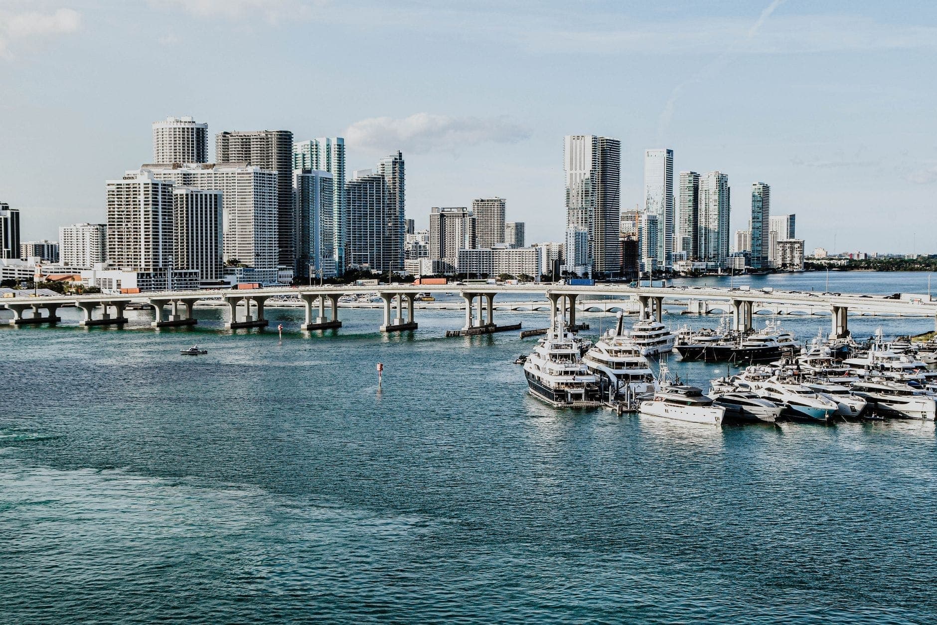 Luxury yachts docked in the foreground with the Miami downtown skyline and Biscayne Bay clearly visible on a bright day.