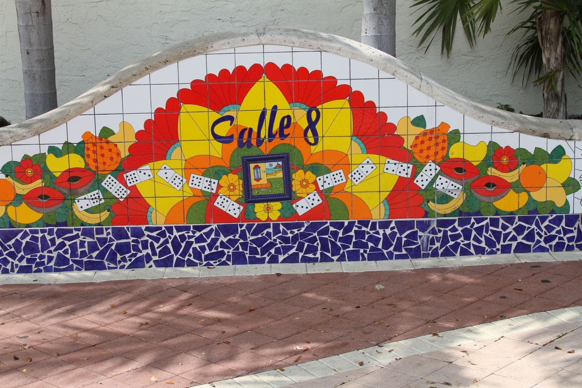 Colorful Calle Ocho mural featuring fruit, dominoes, and the words 'Calle 8', with palm trees behind it in Little Havana, Miami.
