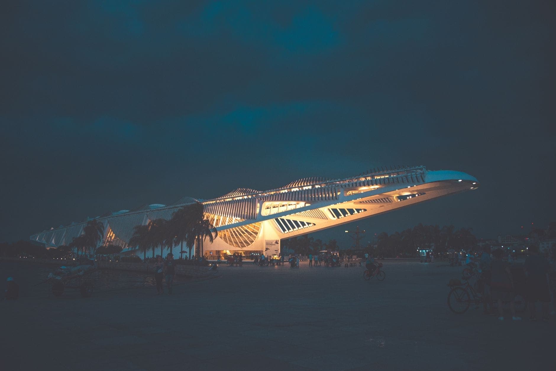 Futuristic white building of the Museum of Science in Miami lit up at night with palm trees and people in the foreground