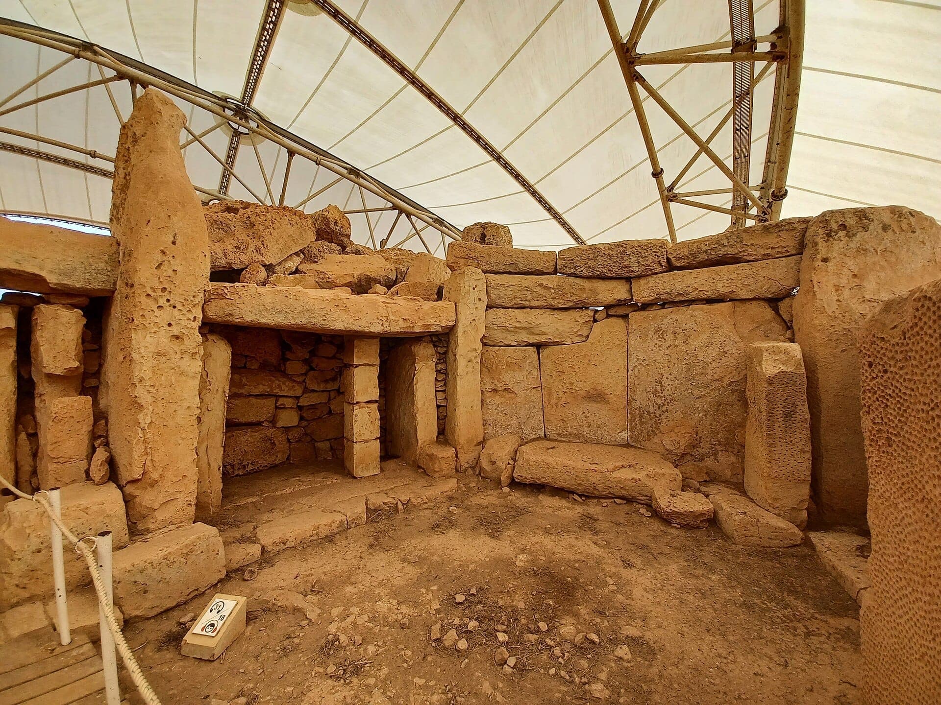 Innenansicht der Mnajdra-Tempel mit Korallenkalksteinblöcken und einem alten Steintor unter einem Schutzdach auf Malta.