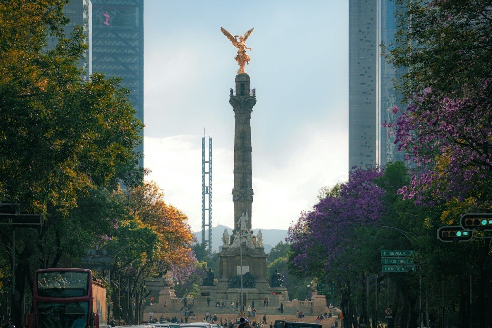 อนุสาวรีย์อังเฮล เด ลา อินเดเปนเดนเซีย ตั้งอยู่กลางถนน Reforma รายล้อมด้วยตึกโมเดิร์นและต้นไม้ดอกสีม่วงใต้อากาศที่ดูทรงพลัง