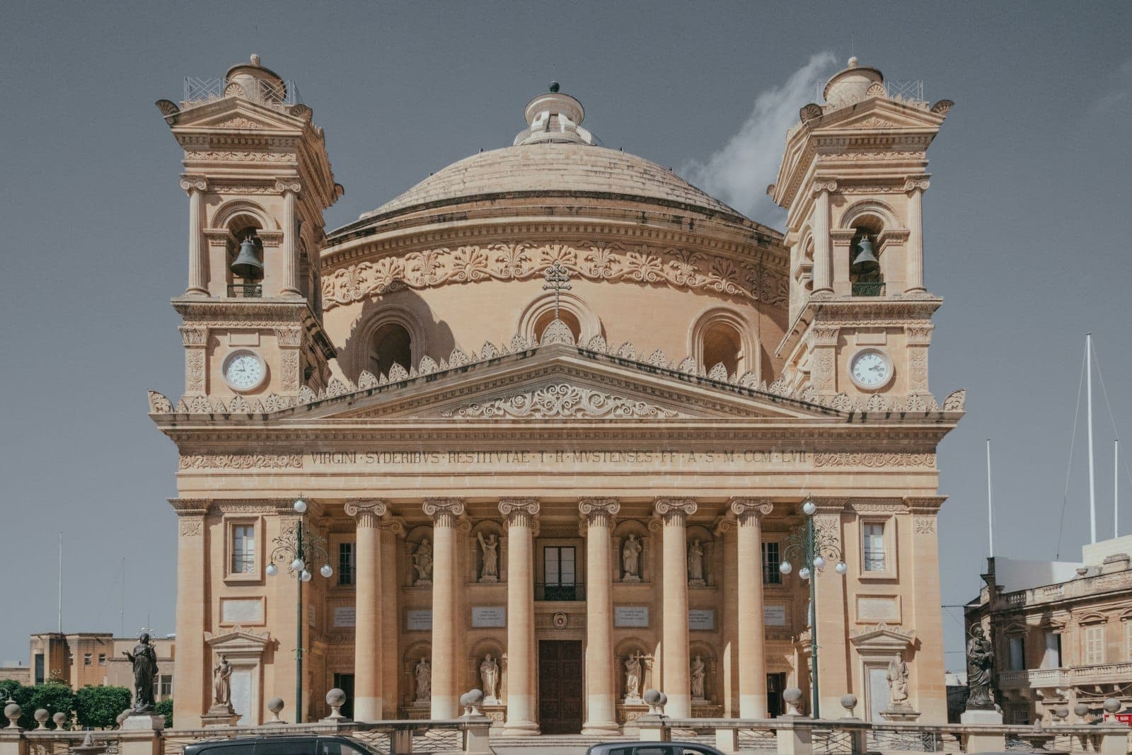 Frontansicht der ikonischen Rotunda-Kirche von Mosta unter klarem Himmel, mit ihren mächtigen Säulen und der imposanten Kuppel in der Bildmitte.