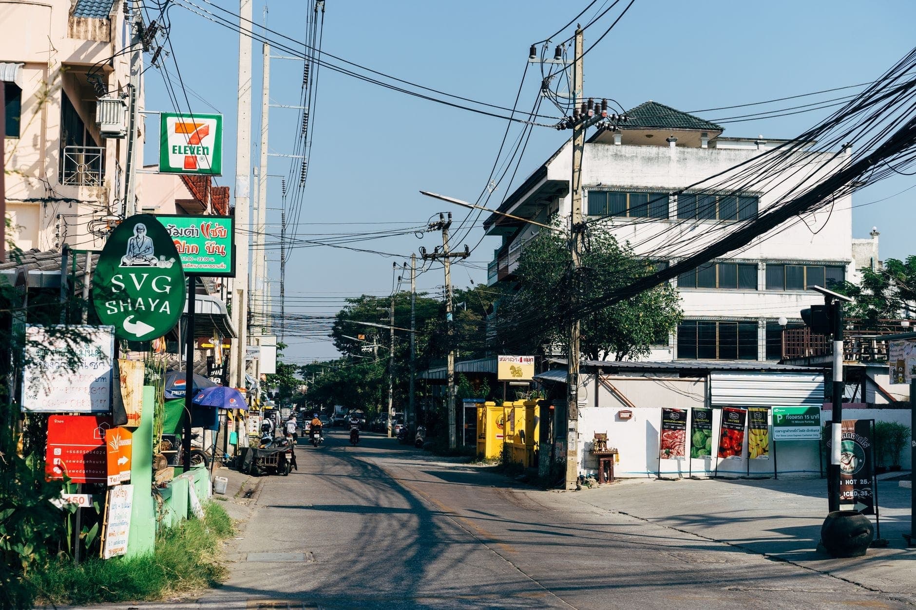 Eine lebhafte Straßenszene in Chiang Mai mit Läden, Thai-Schriftzeichen und Gebäuden unter einem klaren blauen Himmel – genau die Atmosphäre rund um die lokalen Muay-Thai-Gyms.