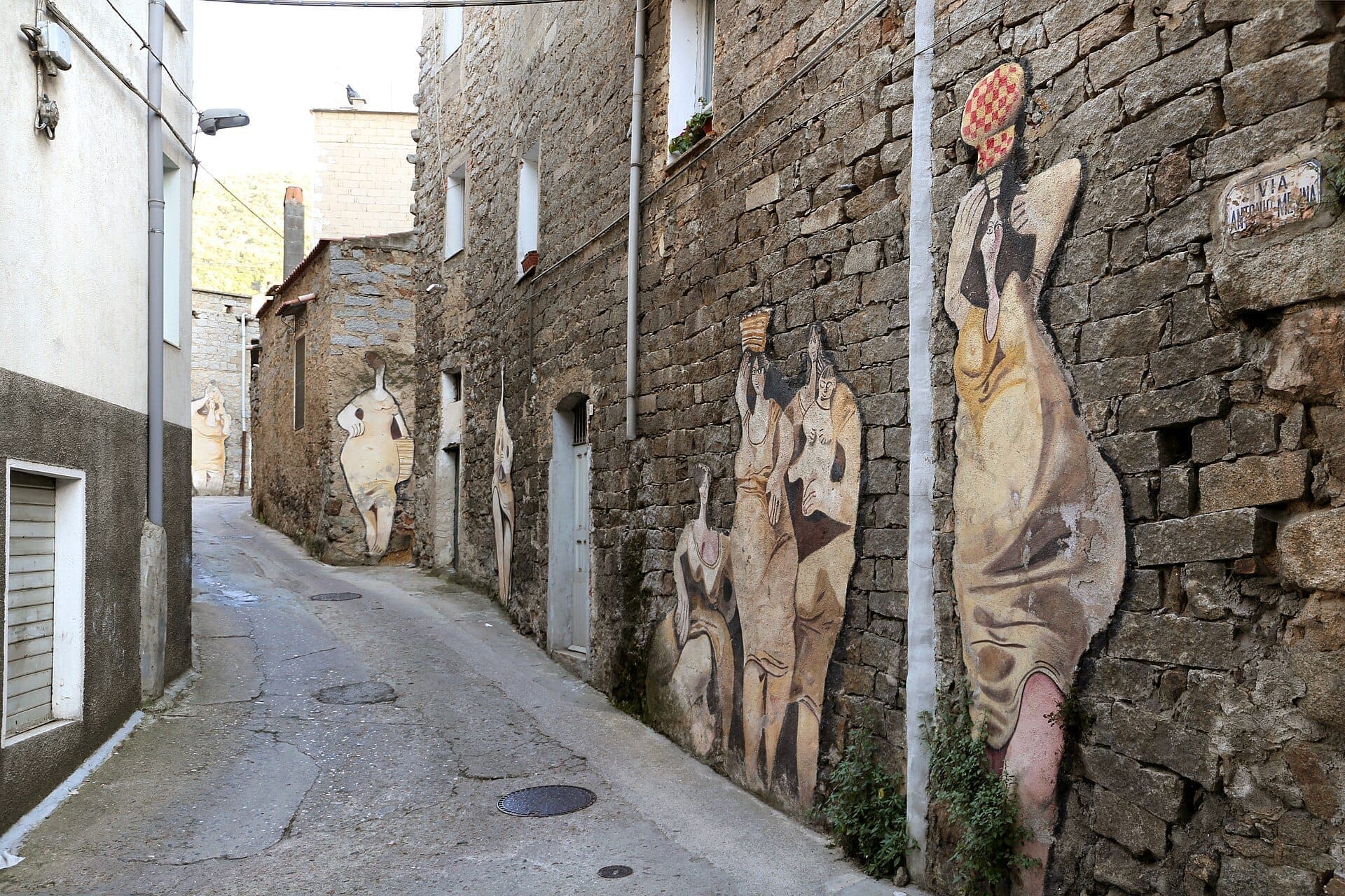 Vista de la calle de los edificios de piedra de Orgosolo decorados con grandes murales estilizados de personas, parte de los famosos Murales di Orgosolo.