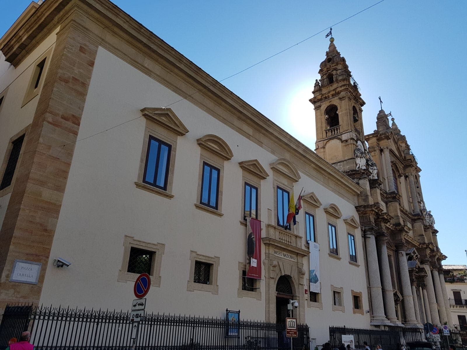 Museo Archeologico Regionale Antonino Salinas di Palermo, menampilkan fasad megah abad ke-17 dan menara lonceng gereja di bawah langit biru yang cerah.