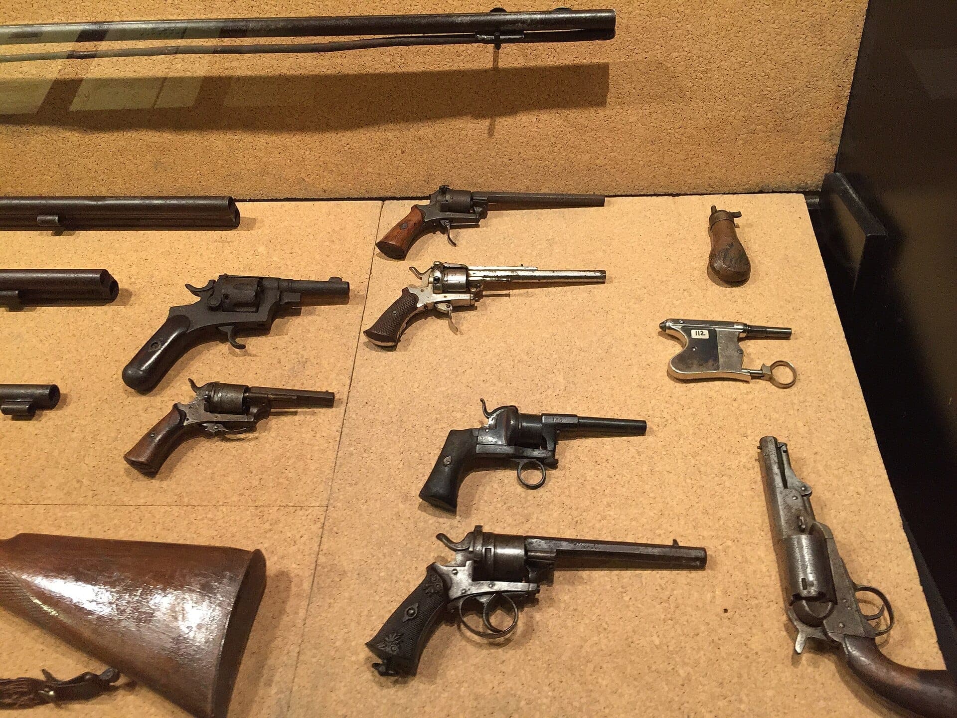 Vitrina en el interior del Museo del Banditismo di Aggius que muestra una colección de pistolas antiguas y armas de fuego sobre un fondo de corcho.