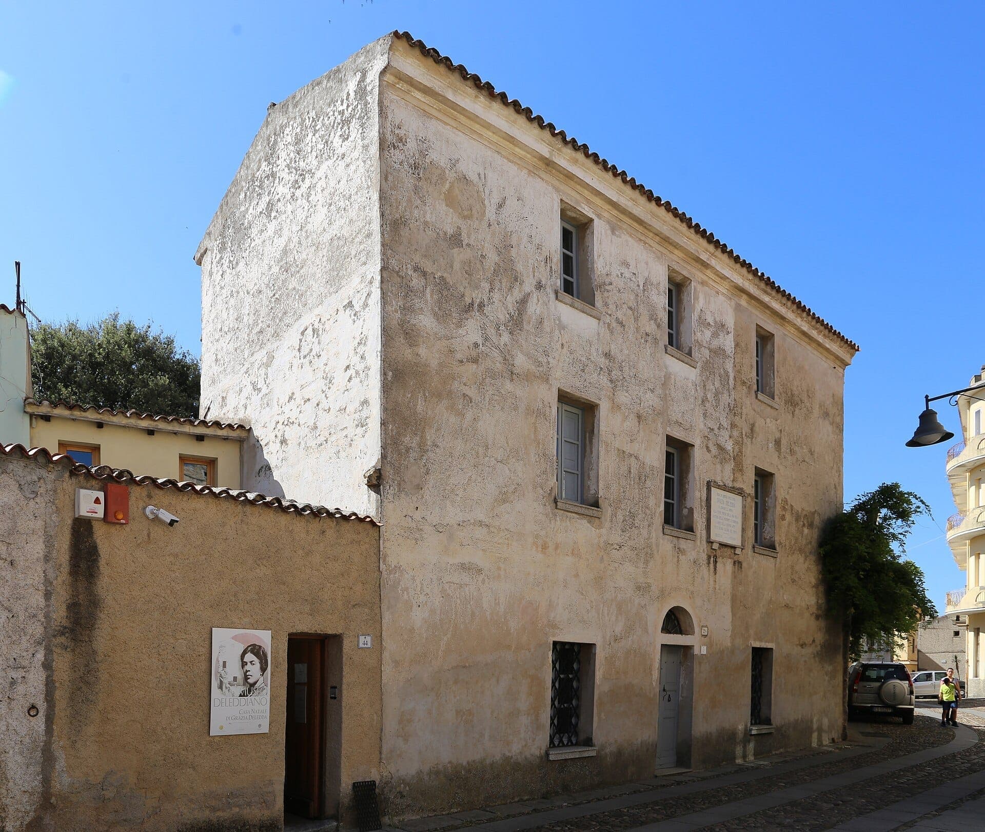 La fachada de piedra desgastada del Museo Deleddiano y sus ventanas grises bajo un cielo azul despejado en el distrito histórico de Nuoro.
