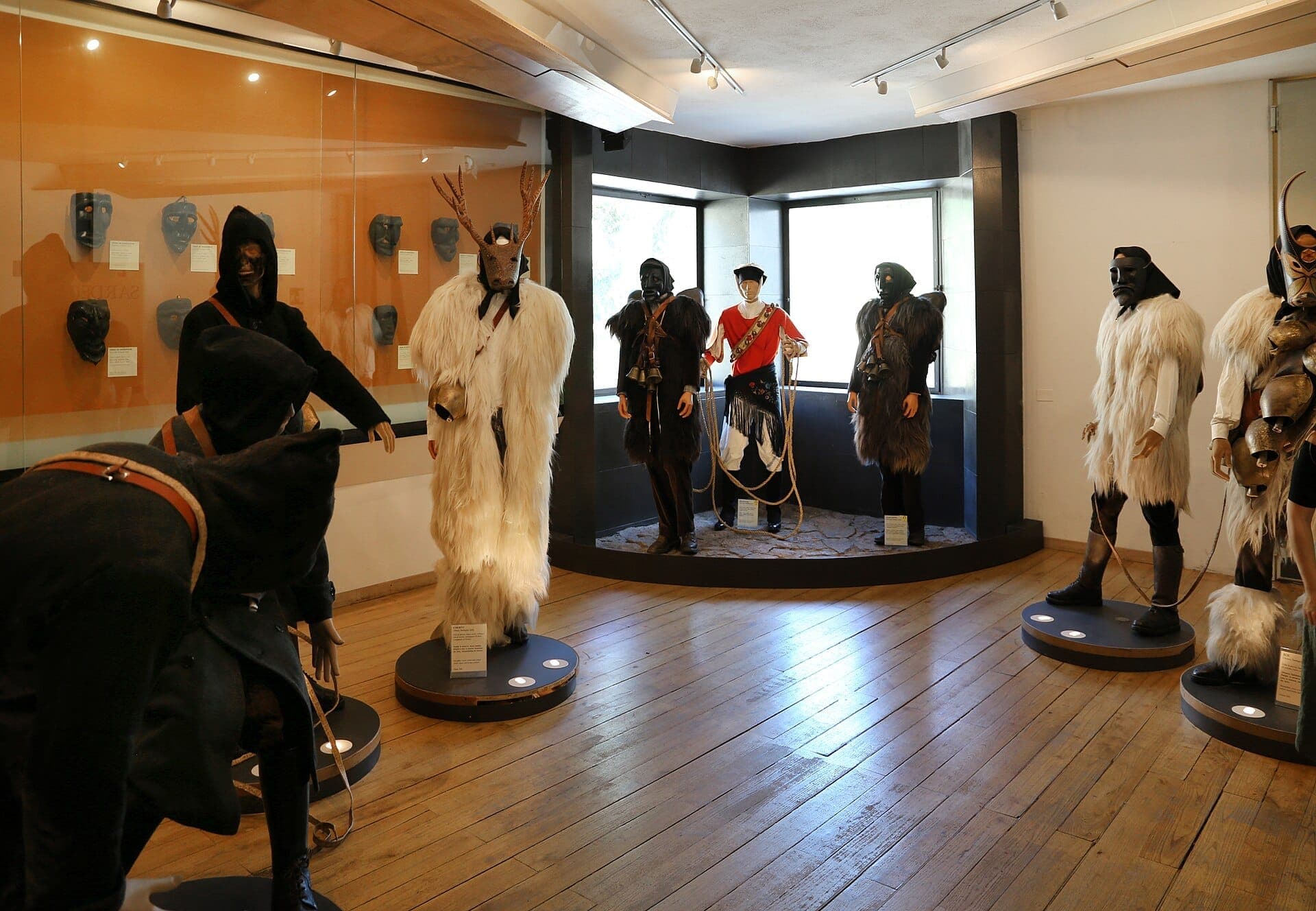 Sala de exposición en el Museo delle Maschere Mediterranee con trajes y máscaras tradicionales del carnaval sardo en maniquíes, con suelos de madera y luz natural.