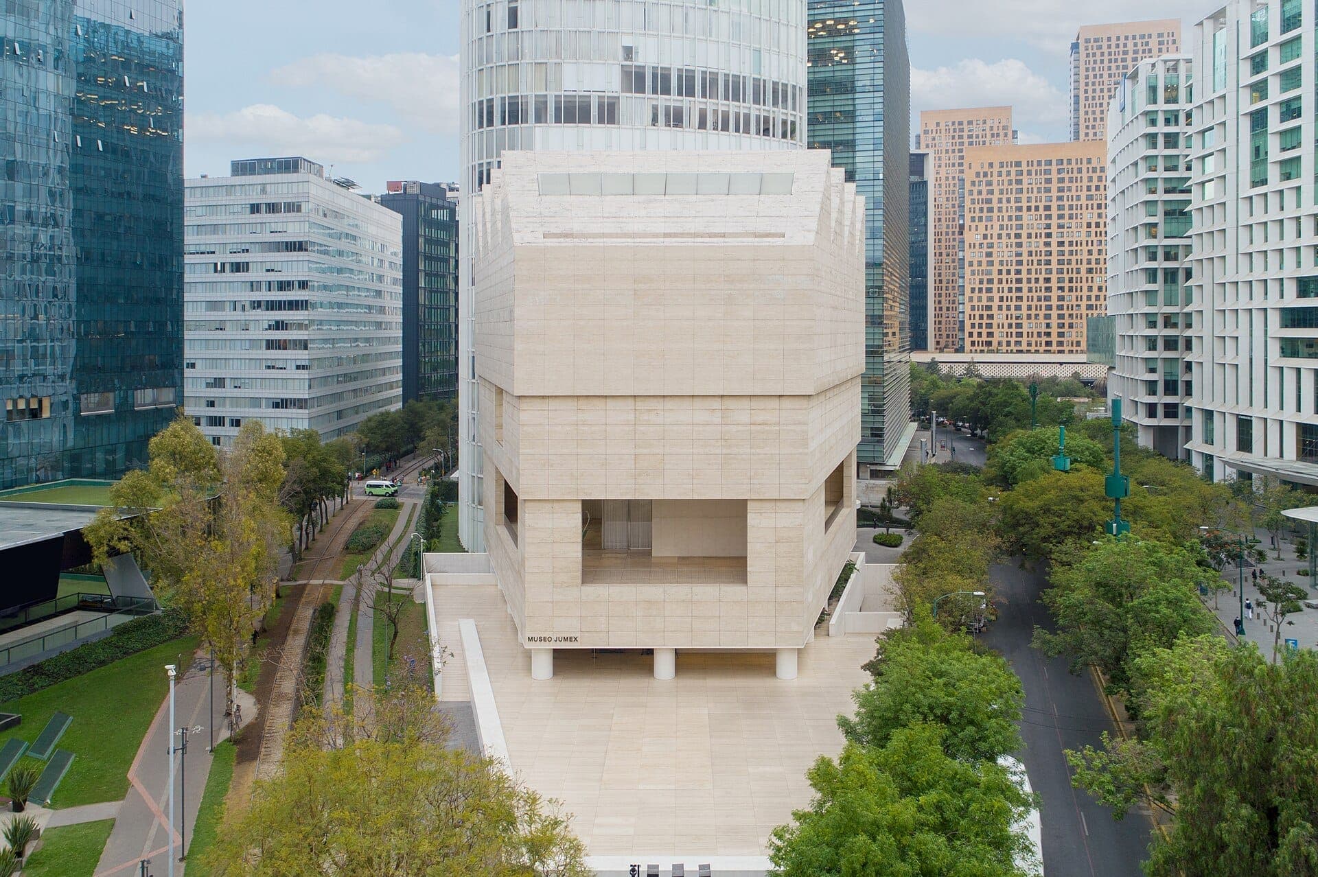 มุมมองด้านหน้าของ Museo Jumex อาคารหินสีเบจสมัยใหม่ที่ล้อมรอบด้วยตึกระฟ้ากระจกและถนนเรียงรายด้วยต้นไม้ใน Polanco เม็กซิโกซิตี้