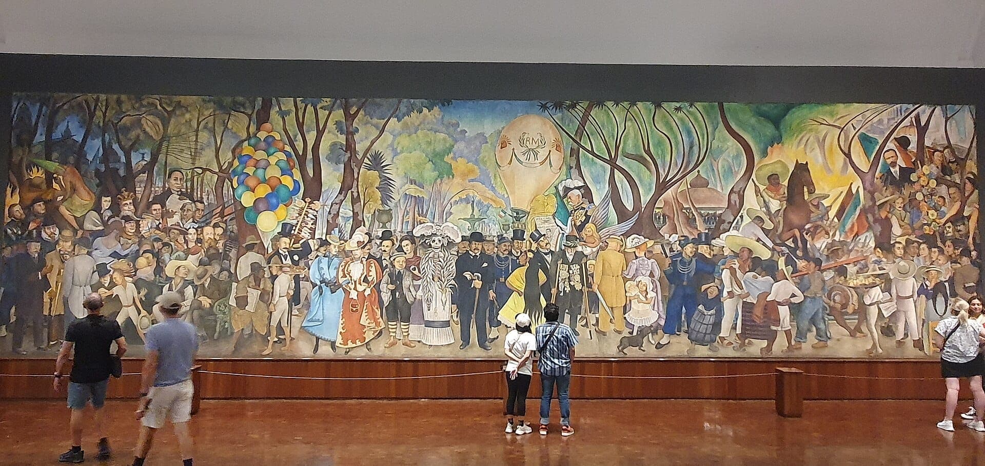 นักท่องเที่ยวยืนอยู่หน้าภาพจิตรกรรมฝาผนังอันสดใสของ Diego Rivera ภายใน Museo Mural Diego Rivera ซึ่งมีภาพบุคคลสำคัญทางประวัติศาสตร์ของเม็กซิโกในฉากขนาดใหญ่สีสันสดใส
