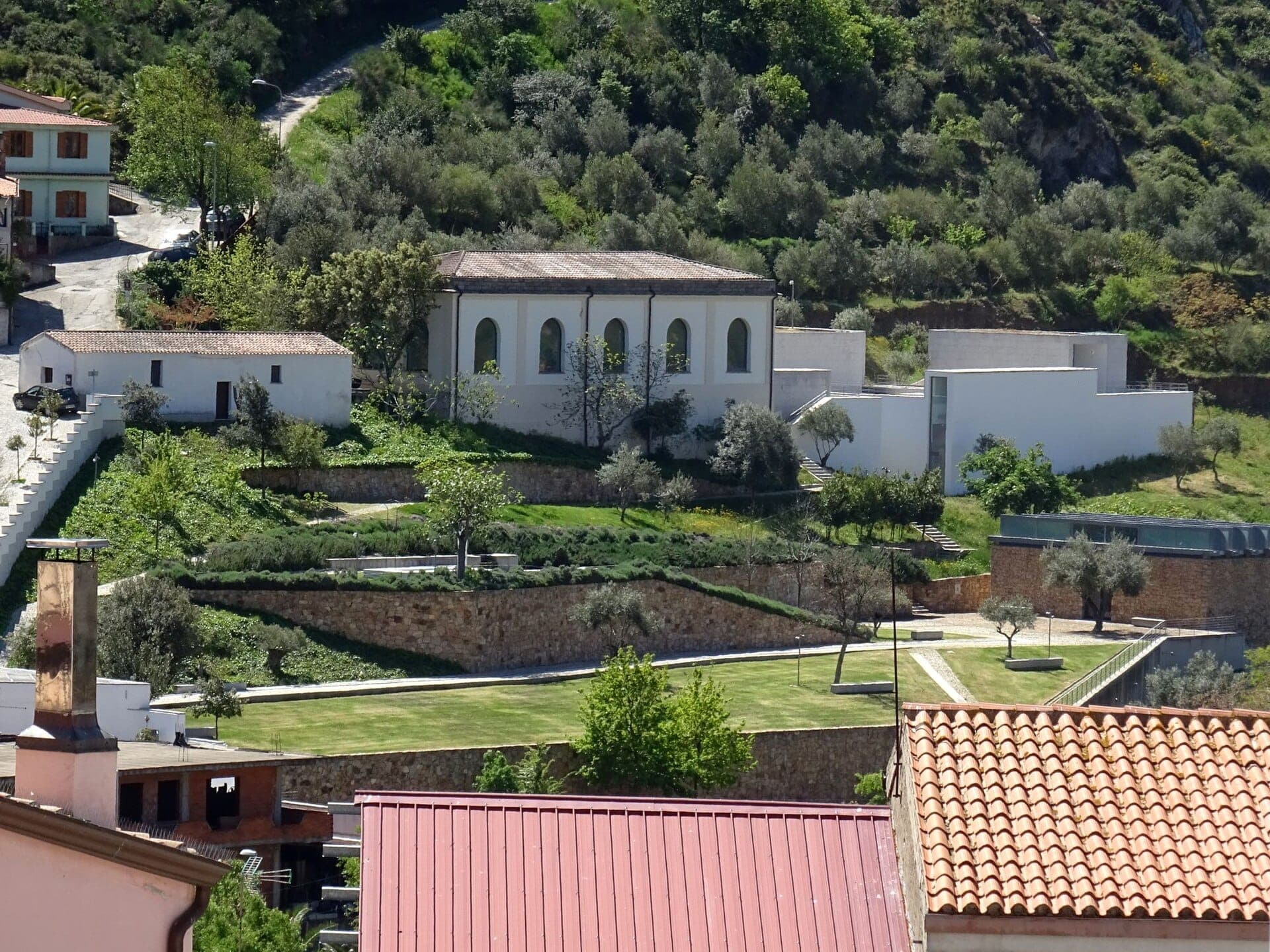 Vista exterior del Museo Nivola en Orani, Cerdeña, rodeado de jardines en terrazas, edificios blancos y exuberantes colinas verdes.