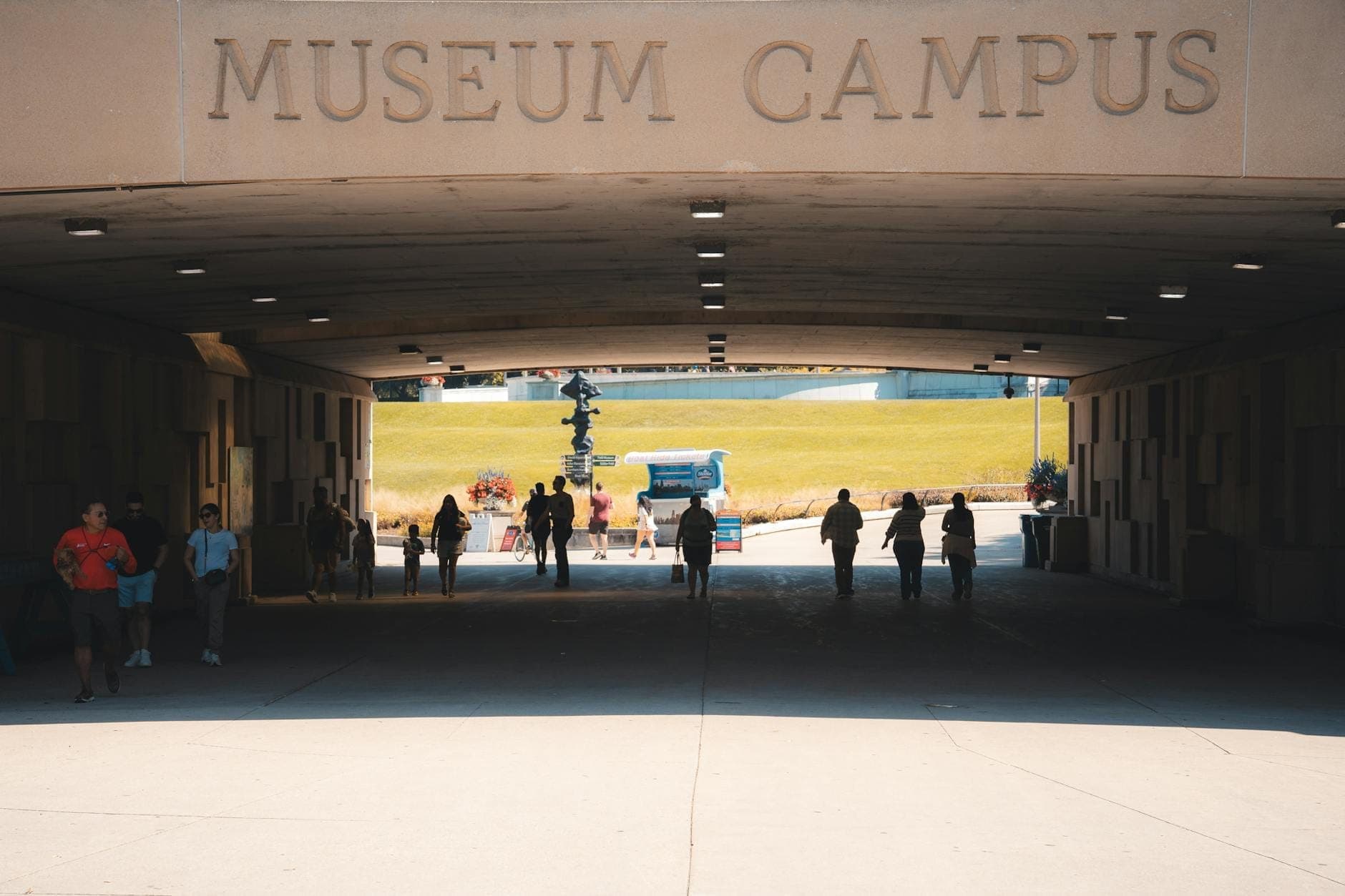 People walking through a tunnel entrance labeled 'Museum Campus' toward a sunny outdoor area, representing Chicago's Museum Campus and its inviting atmosphere.