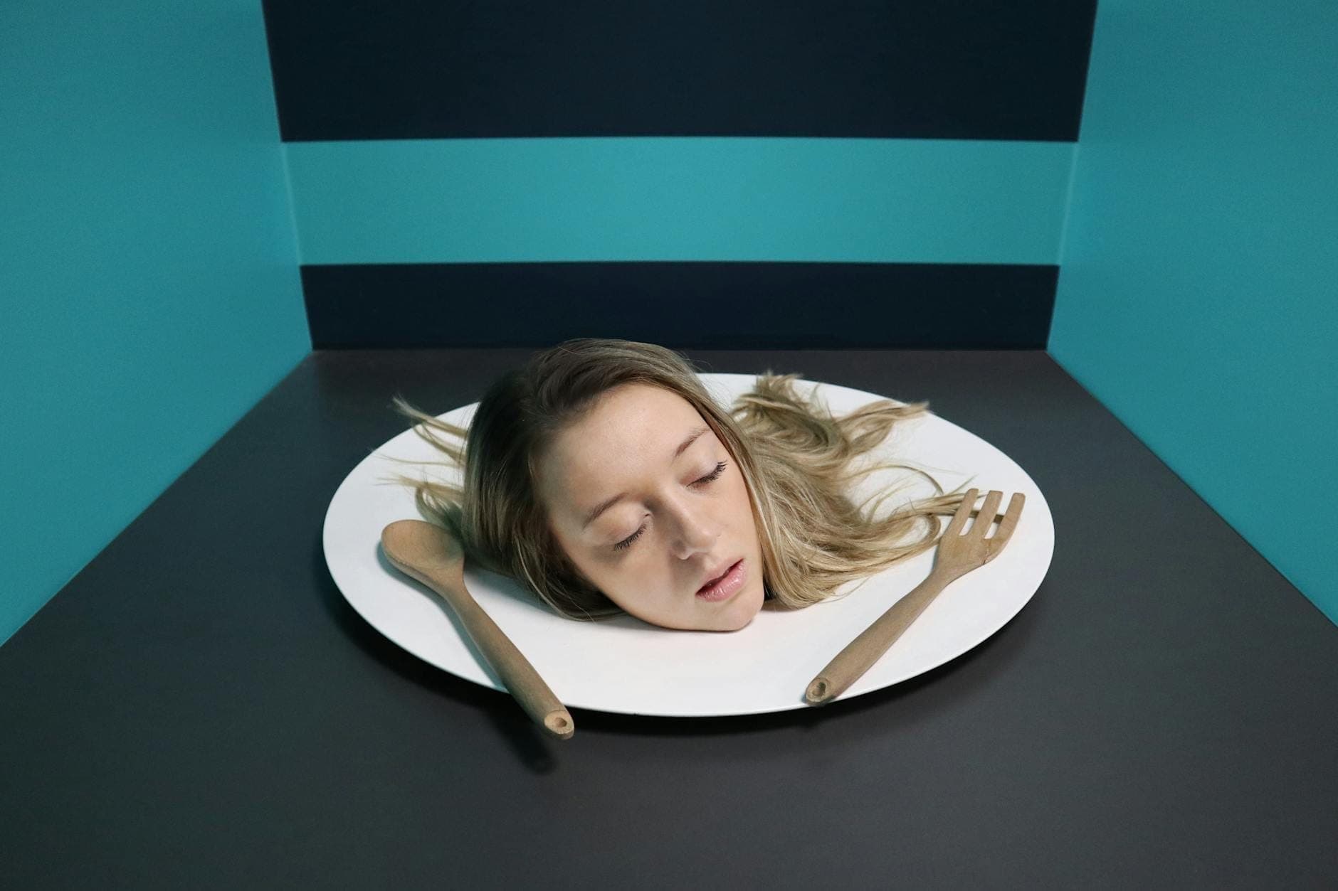 Un'installazione giocosa in cui una persona sembra avere solo la testa posata su un vassoio, circondata da pareti a strisce turchesi, all'interno del Museo delle Illusioni di Spalato.