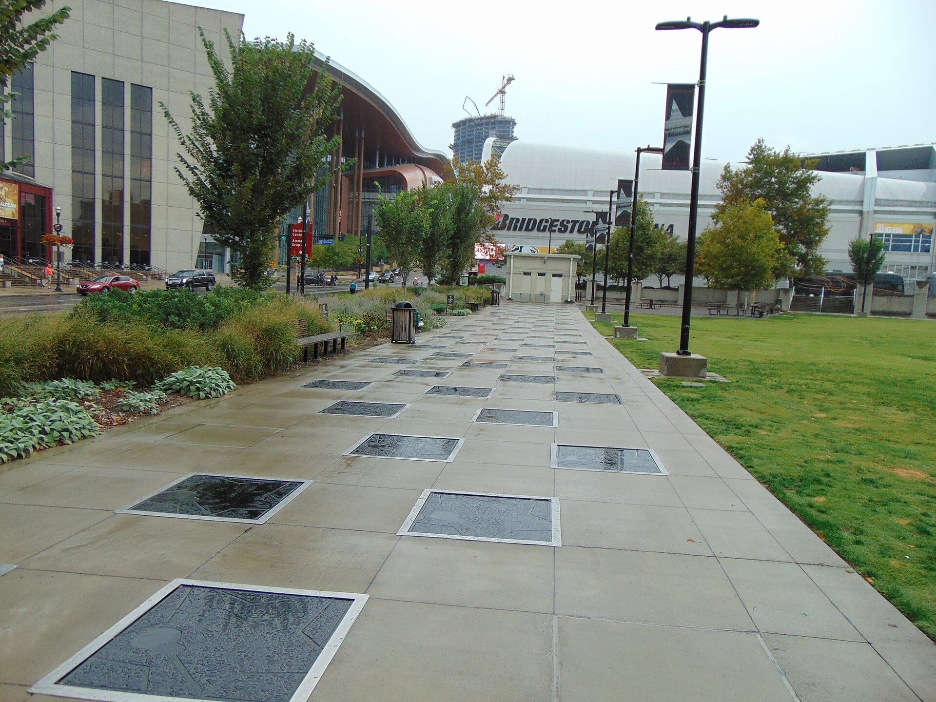Concrete walkway lined with name plaques at Music City Walk of Fame Park in downtown Nashville, with modern buildings and greenery on a cloudy day.